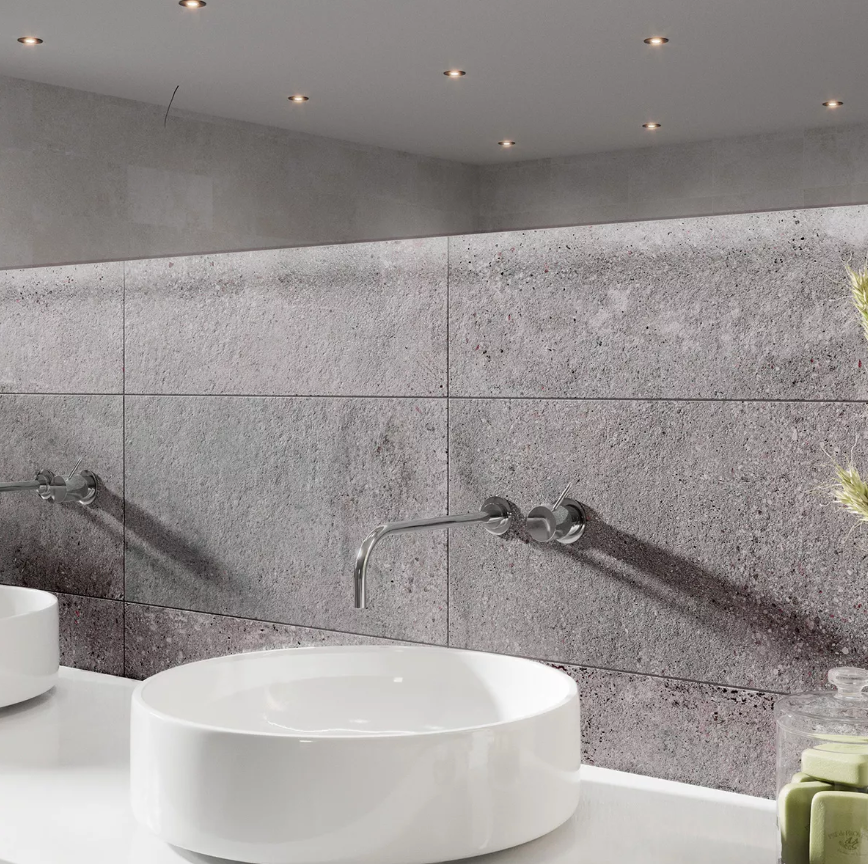 Modern bathroom with gray textured wall tiles, two white vessel sinks, chrome wall-mounted faucets, and reflected ceiling spotlights.