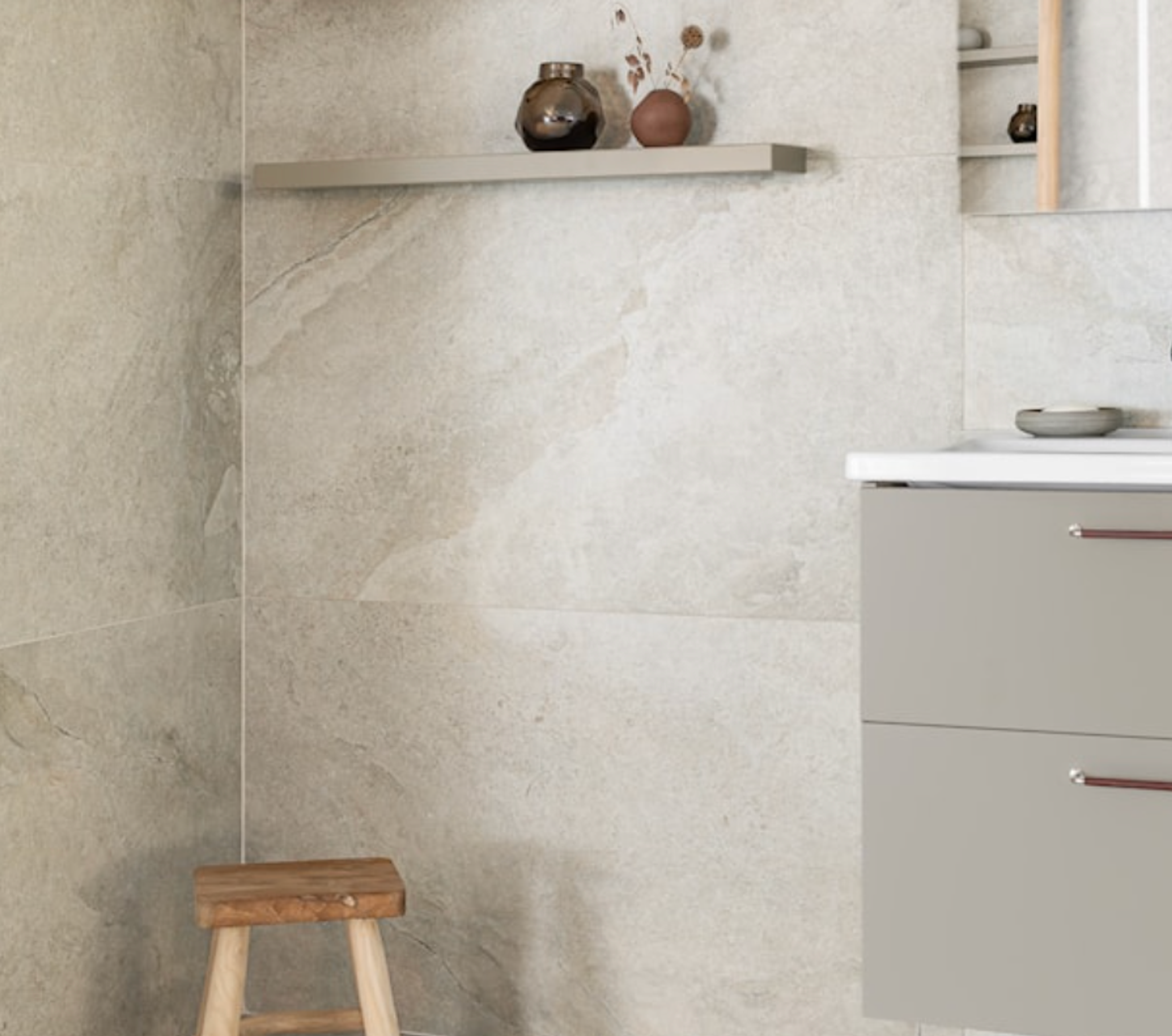 Light-toned tiled bathroom with a wooden stool, a decorated shelf, and a vanity.