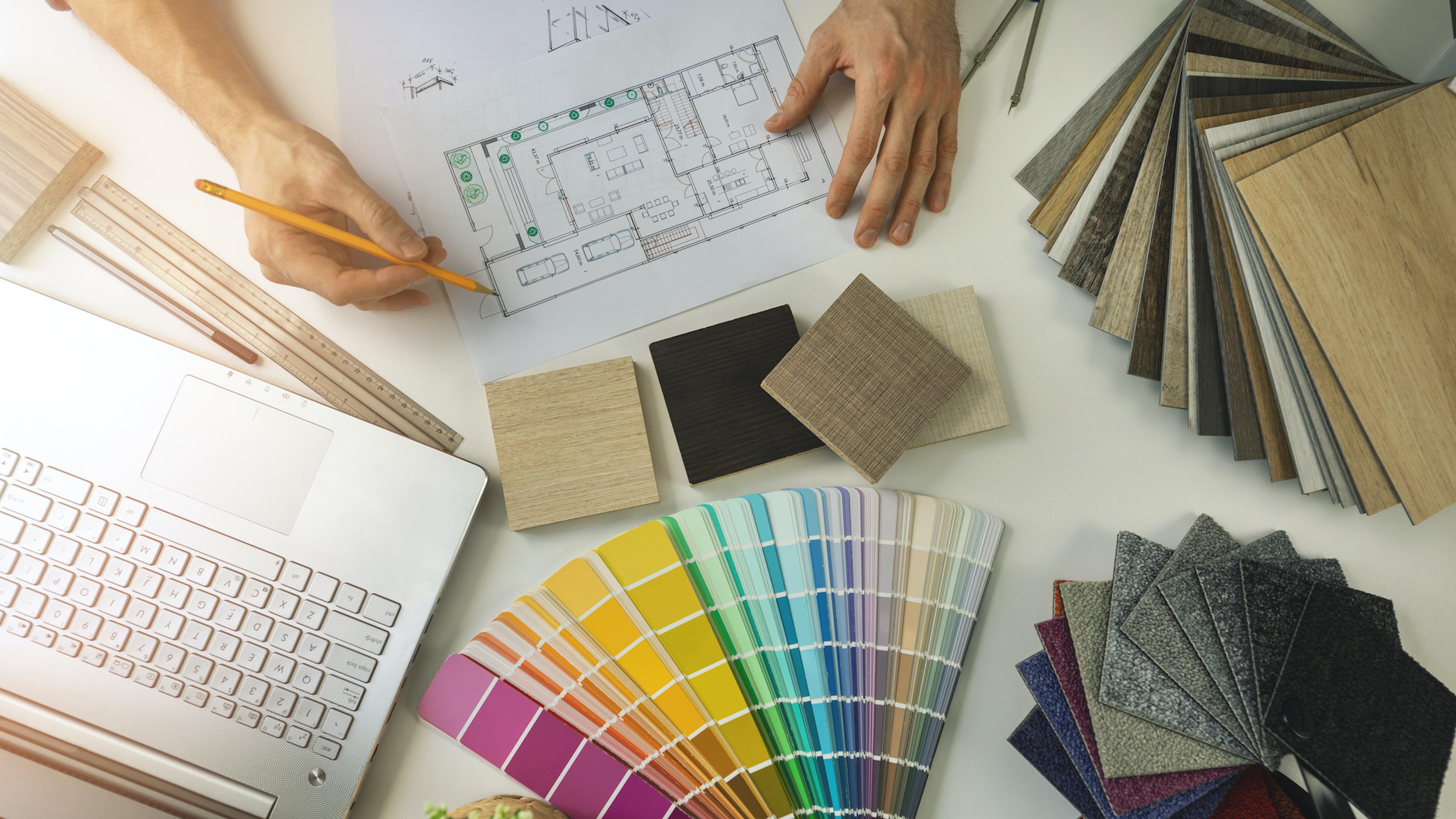Hands reviewing a floor plan with a laptop, color swatches, and various material samples.