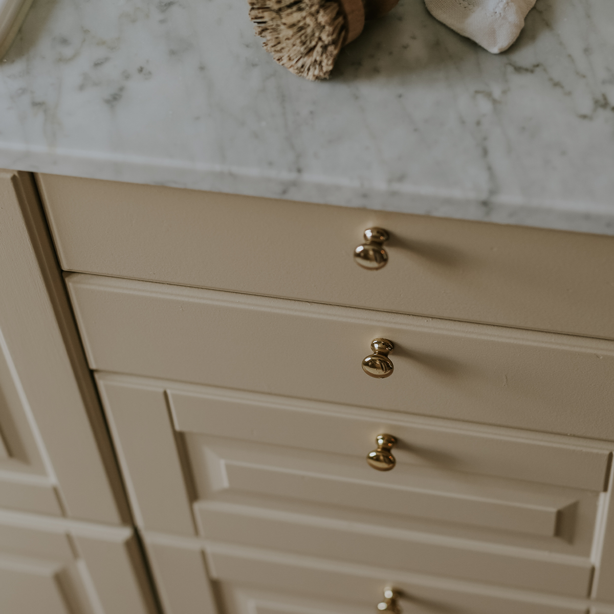 Cream kitchen cabinets with gold knobs below a marble countertop.
