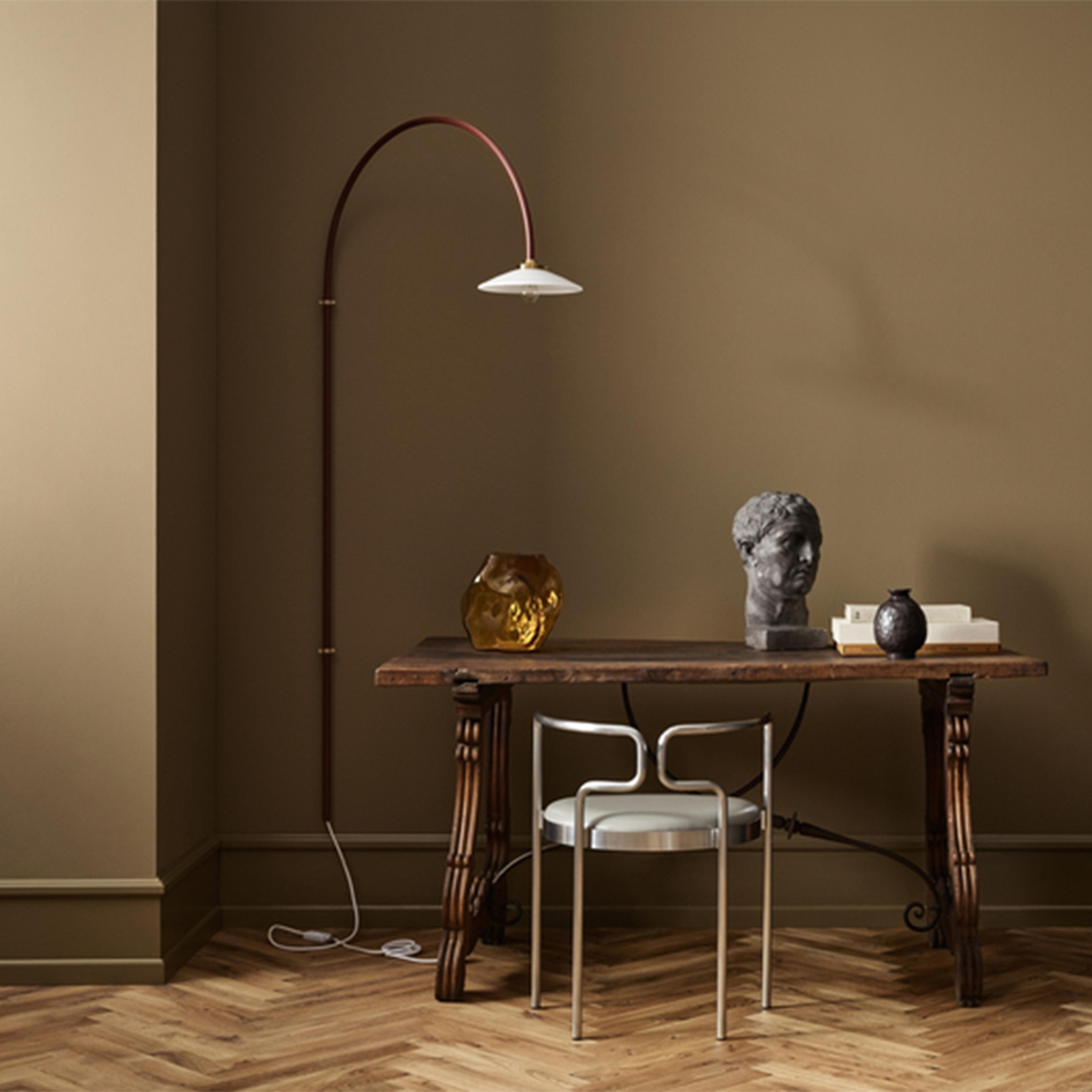 Olive green room with a rustic wooden table, modern silver chair, arched floor lamp, bust, and golden vase.