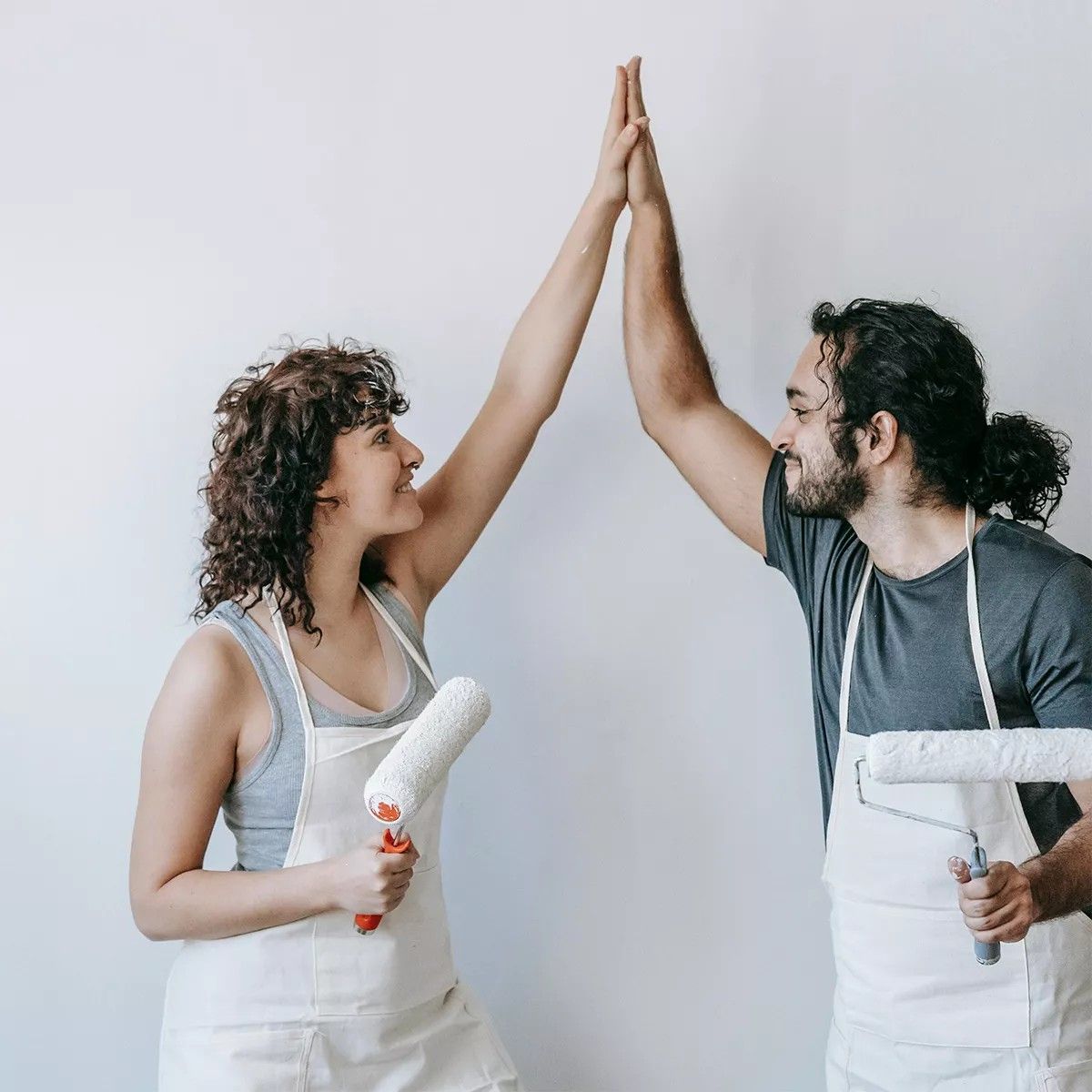 Two smiling people in painting aprons, holding rollers, high-fiving.