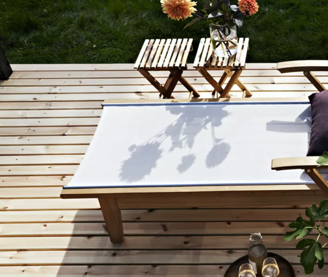 A white lounge chair with a purple cushion on a wooden deck next to a potted fig plant.