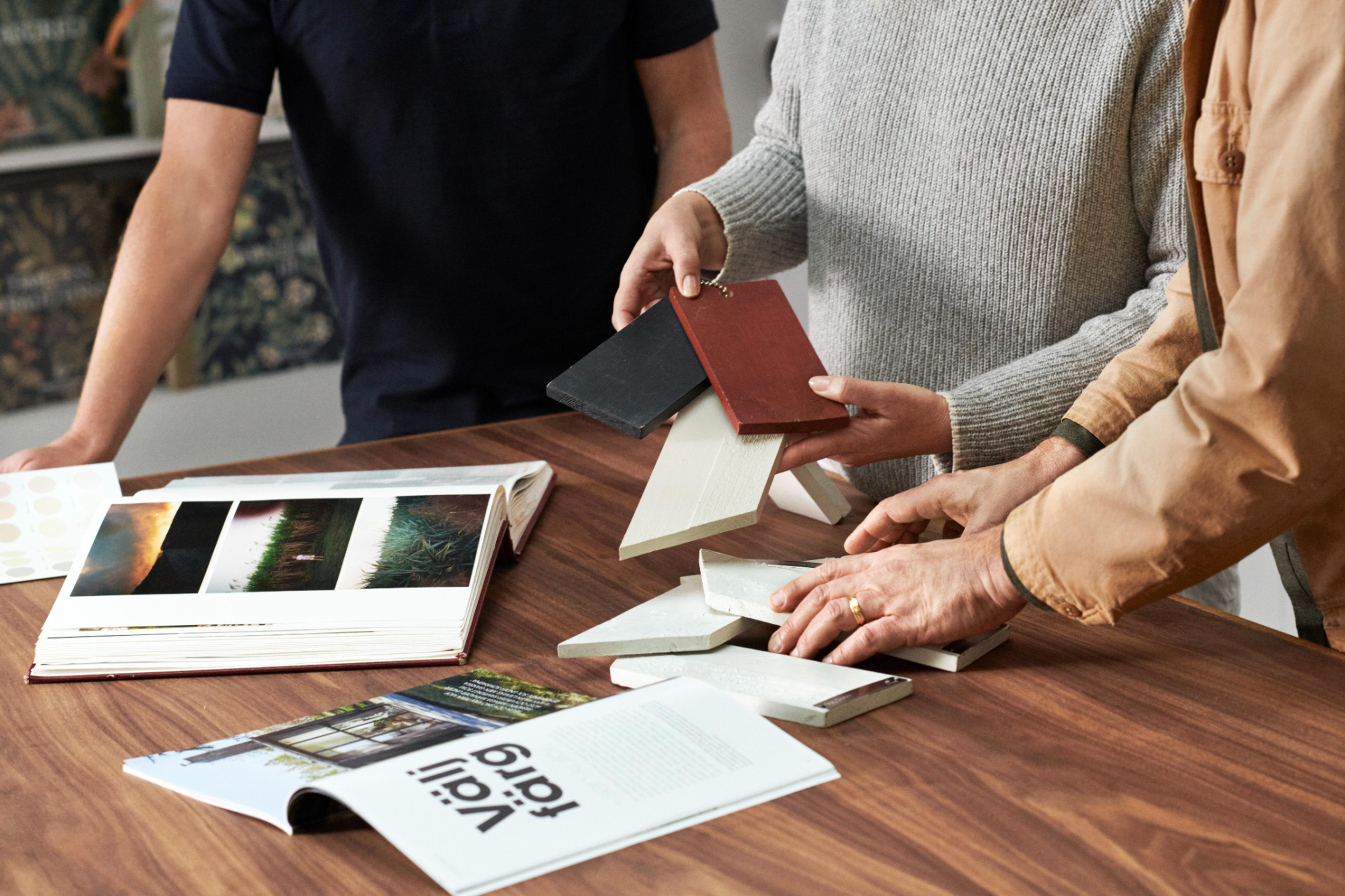 People reviewing material samples and design books on a wooden table.
