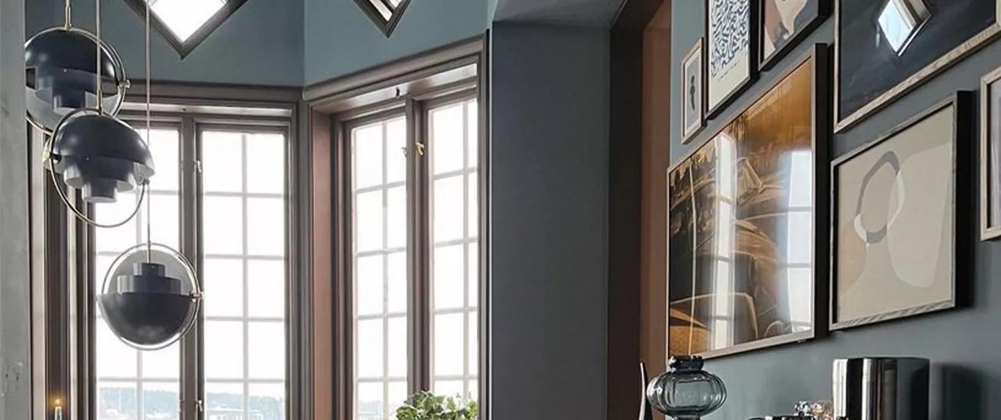 A stylish room interior with a bay window, three modern pendant lights, and a gallery wall.