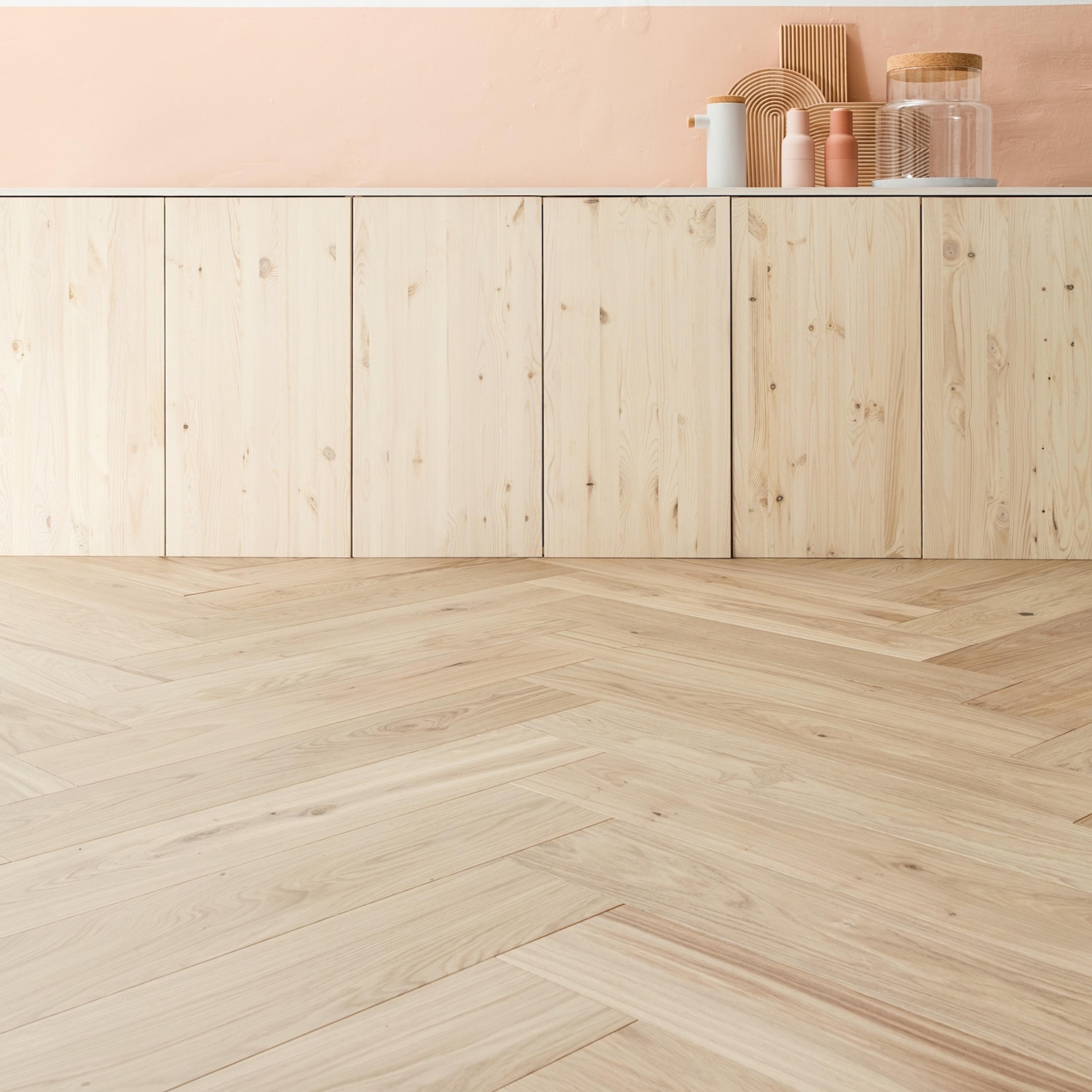 Light wood herringbone floor, natural wood cabinets, a white counter, and a peach wall with minimalist decor.