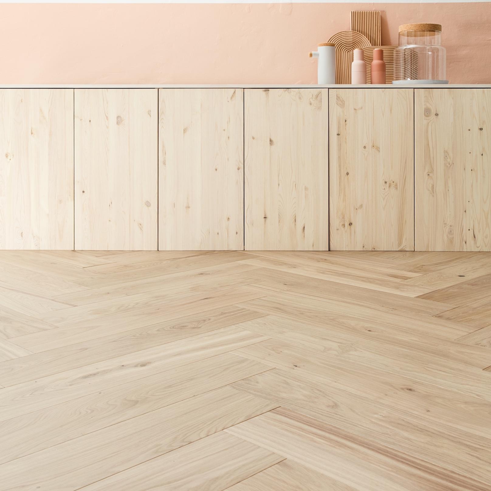 Light wood herringbone floor, natural wood cabinets, a white counter, and a peach wall with minimalist decor.