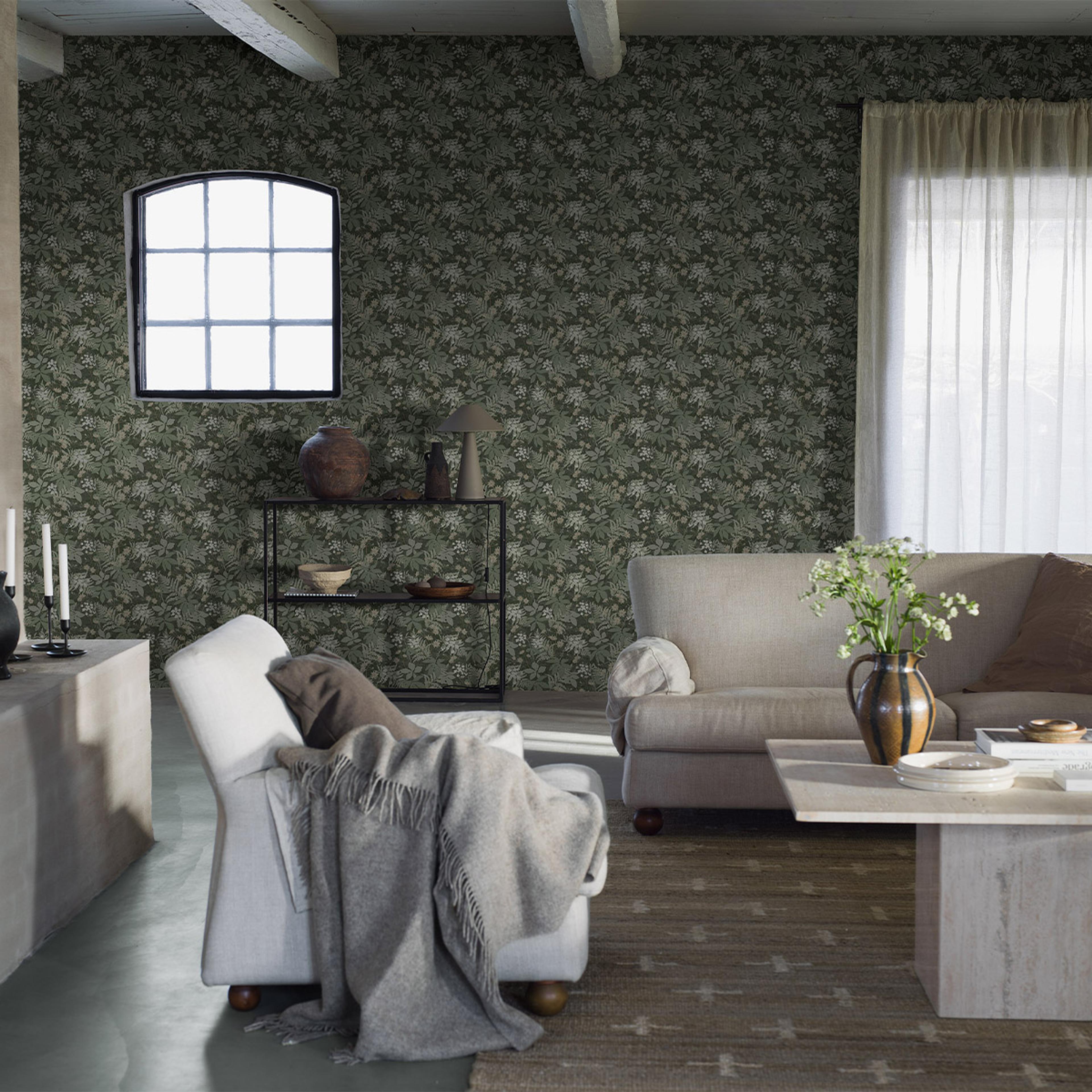 A living room featuring dark green floral wallpaper, an arched window, a beige sofa and armchair, and a coffee table with white flowers.
