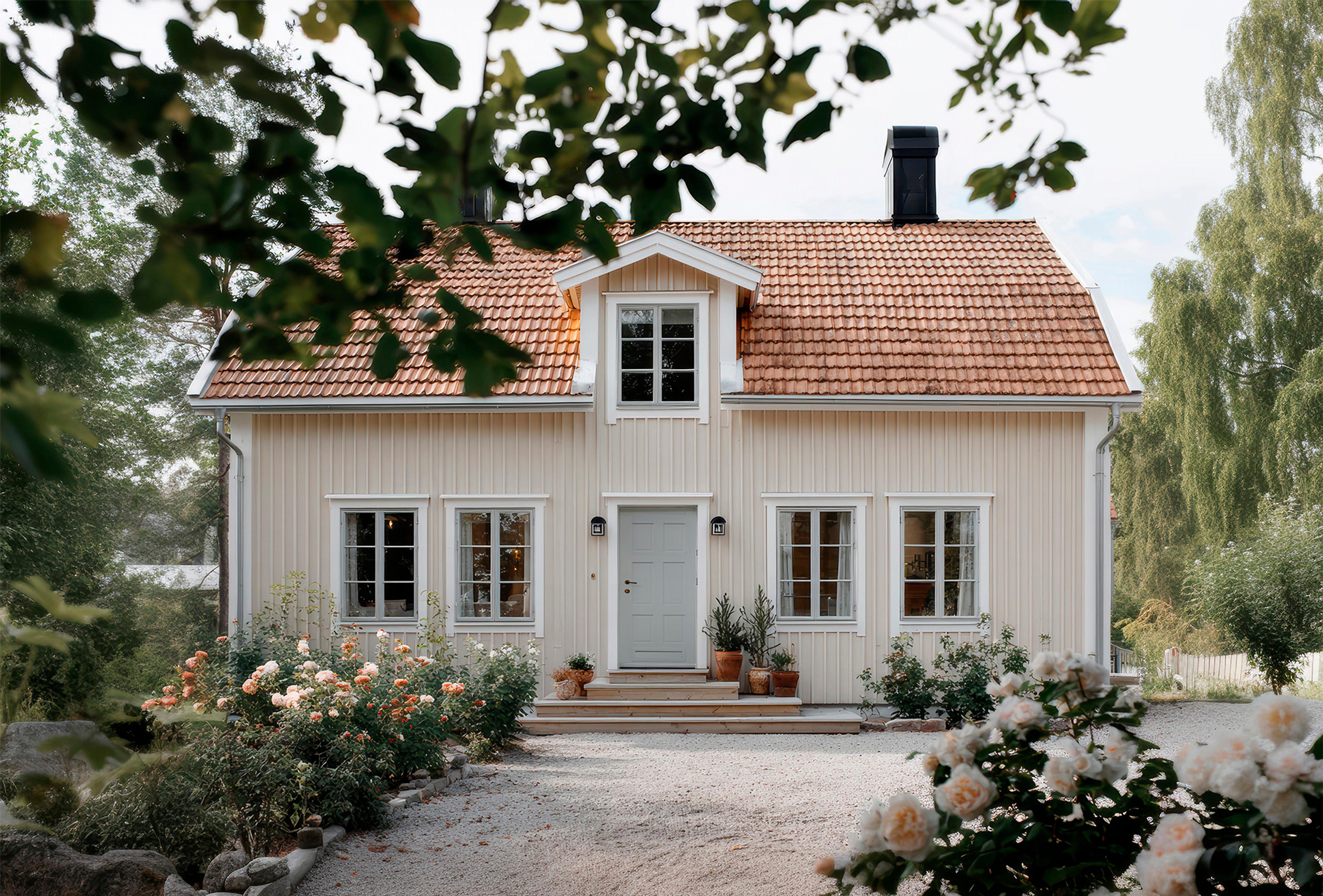 A light yellow house with a red tiled roof, gray front door, and a garden of blooming rose bushes.