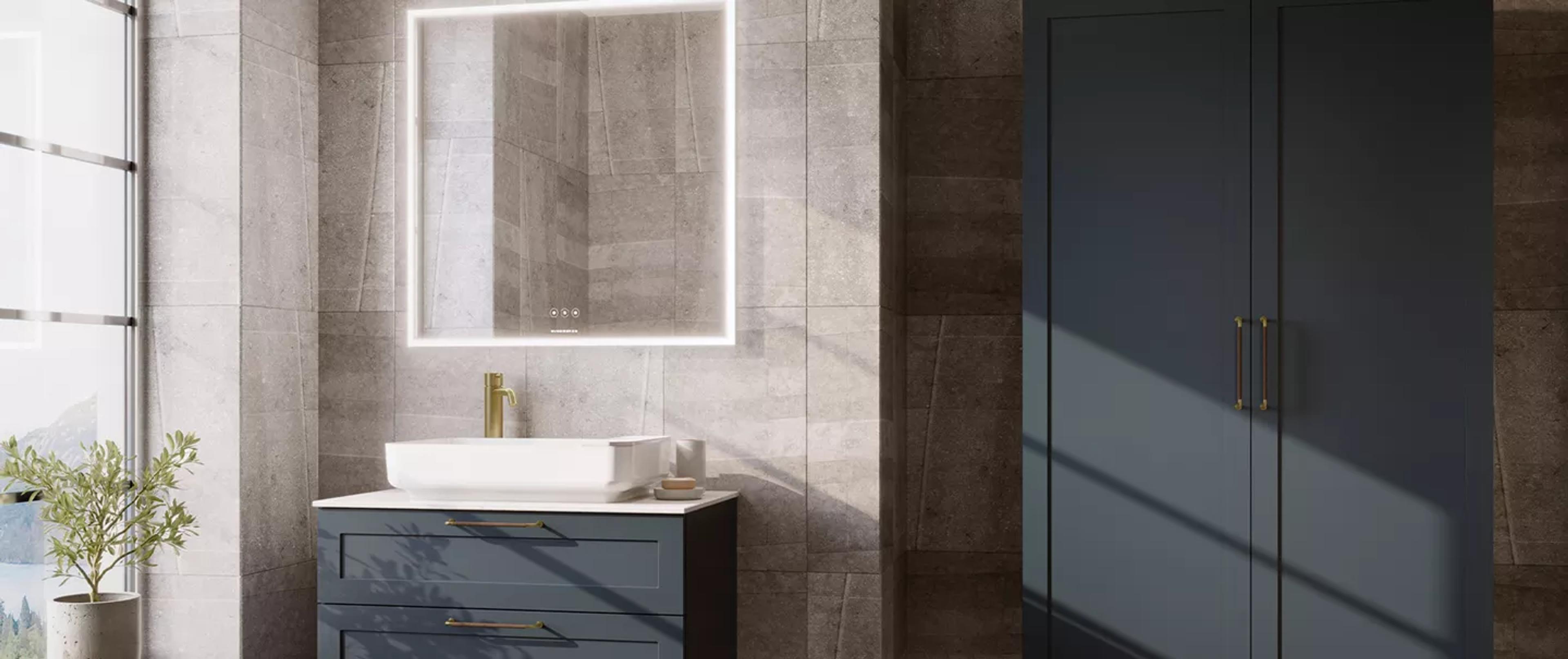 Modern bathroom with a dark blue vanity, white vessel sink, gold faucet, illuminated mirror, and matching dark blue cabinet against gray tiled walls.