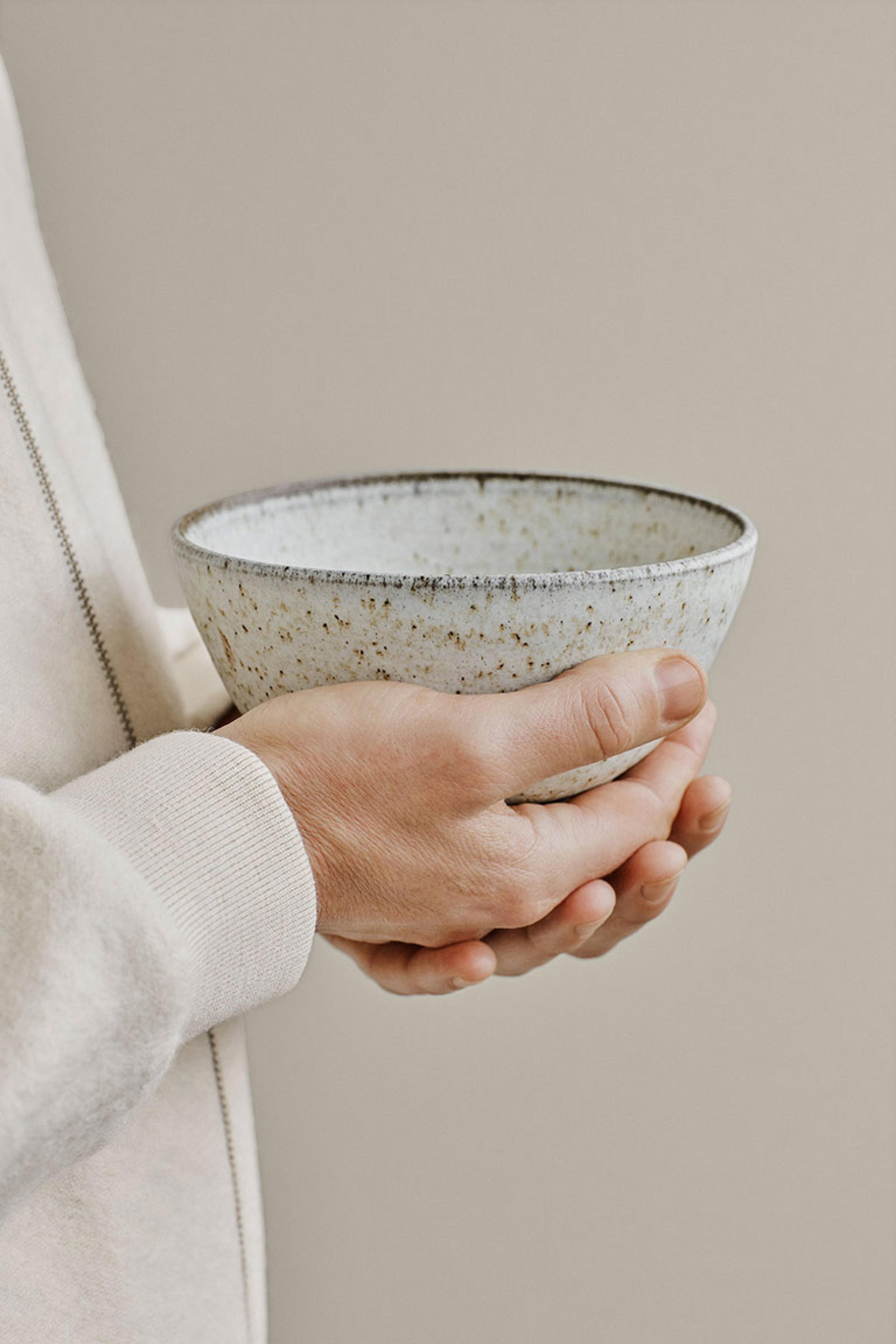 Hands holding a speckled ceramic bowl.