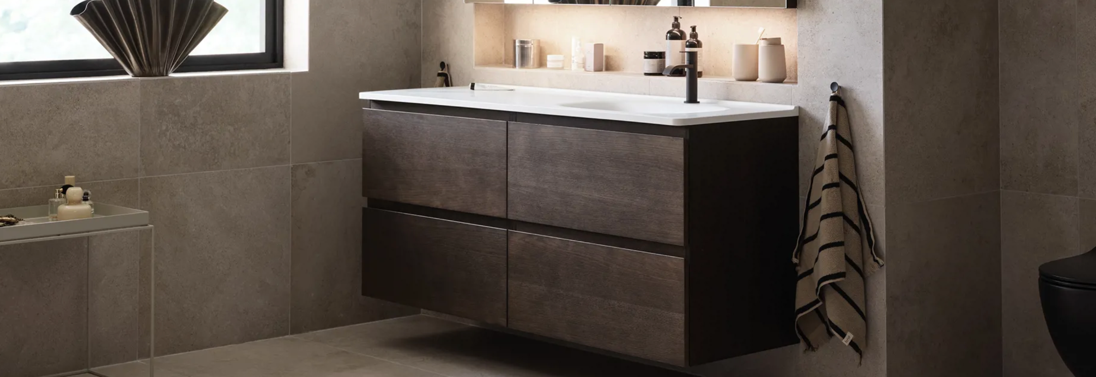 A modern bathroom features a floating dark wood double vanity with white sinks, black faucets, and beige tiled walls.
