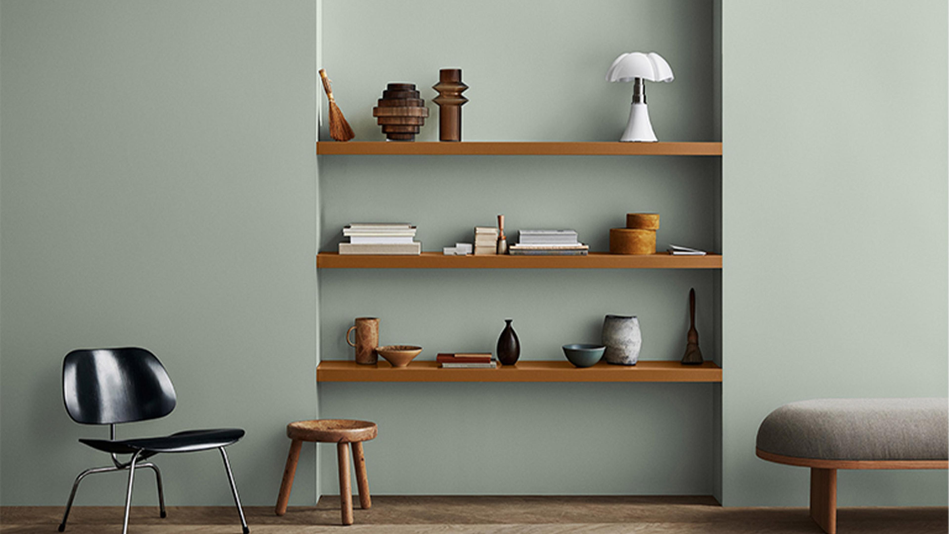 A room with light green walls, wooden shelves holding various decorations, a black chair, and a wooden stool.