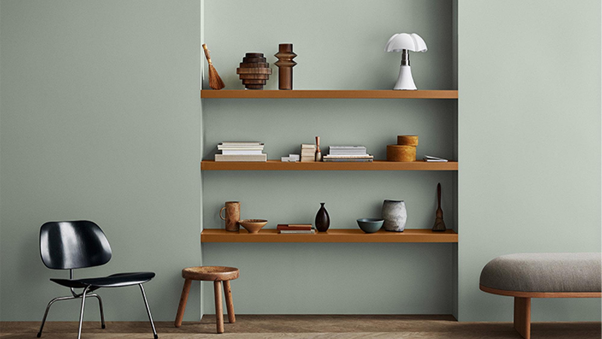 A room with light green walls, wooden shelves holding various decorations, a black chair, and a wooden stool.
