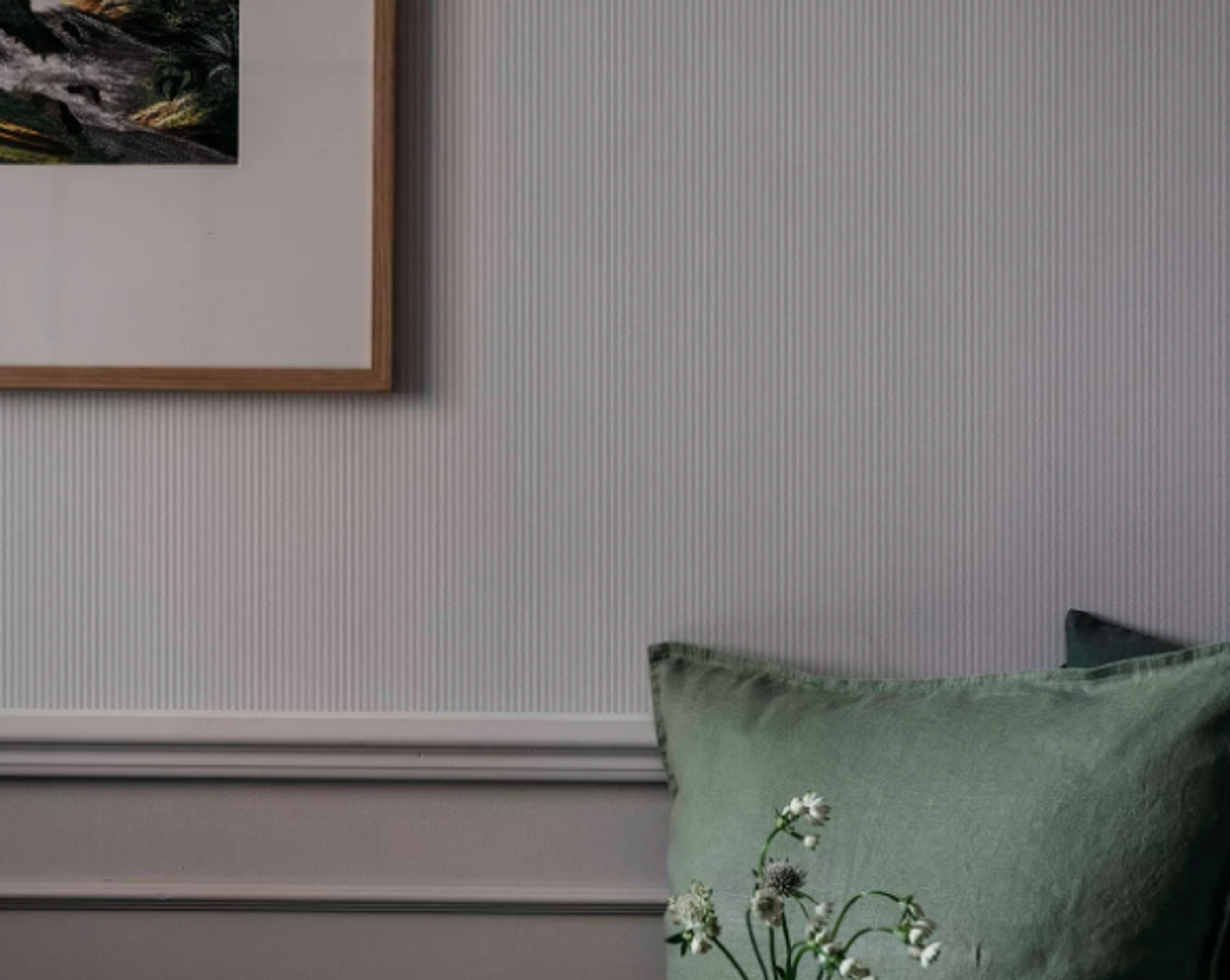A textured grey wall with a framed picture, a green pillow, and white flowers.