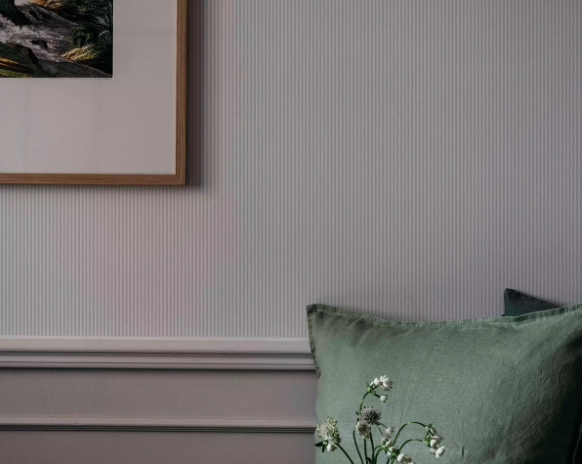 A textured grey wall with a framed picture, a green pillow, and white flowers.