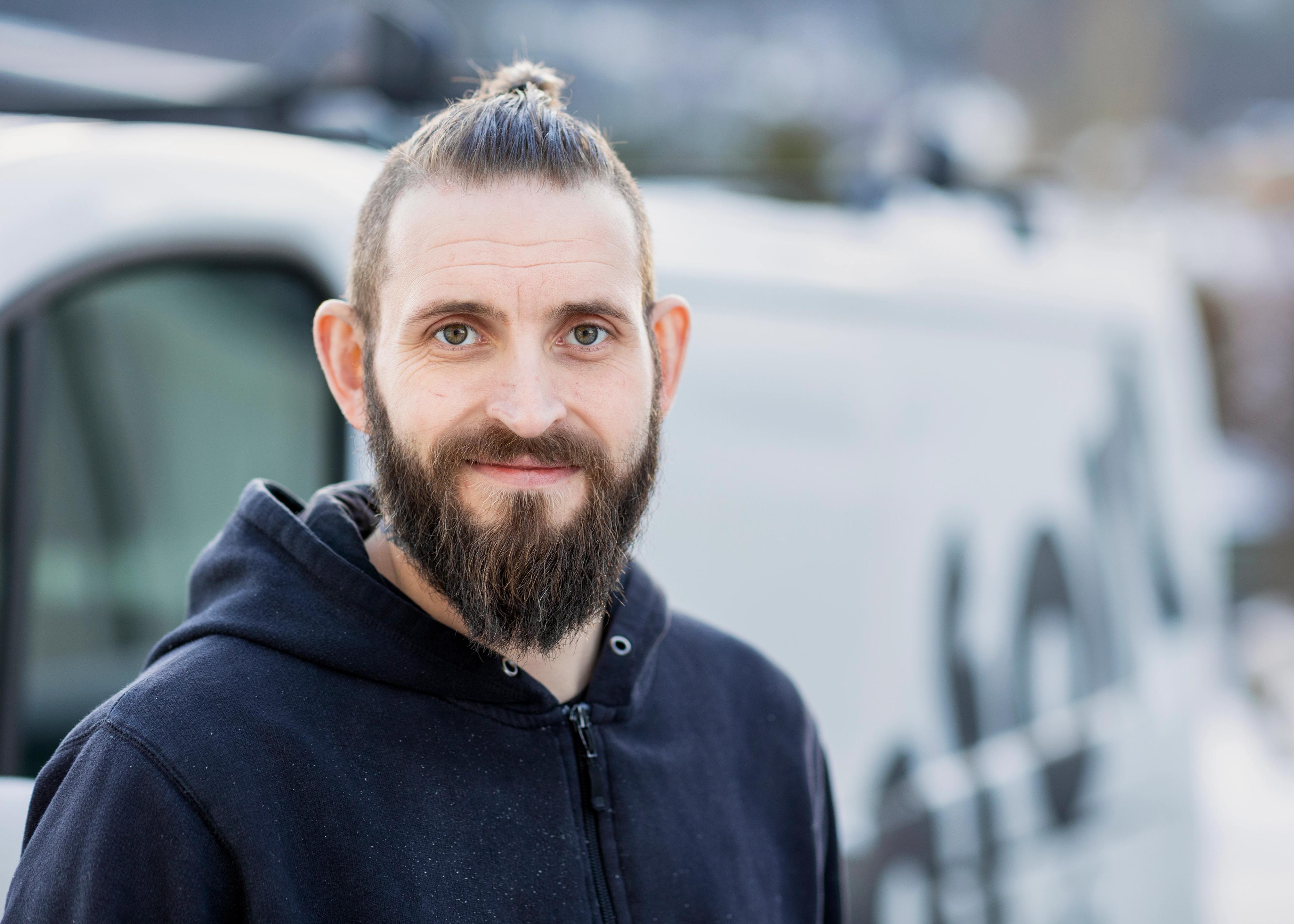 Smilende mann foran en bil det står S-Rør på