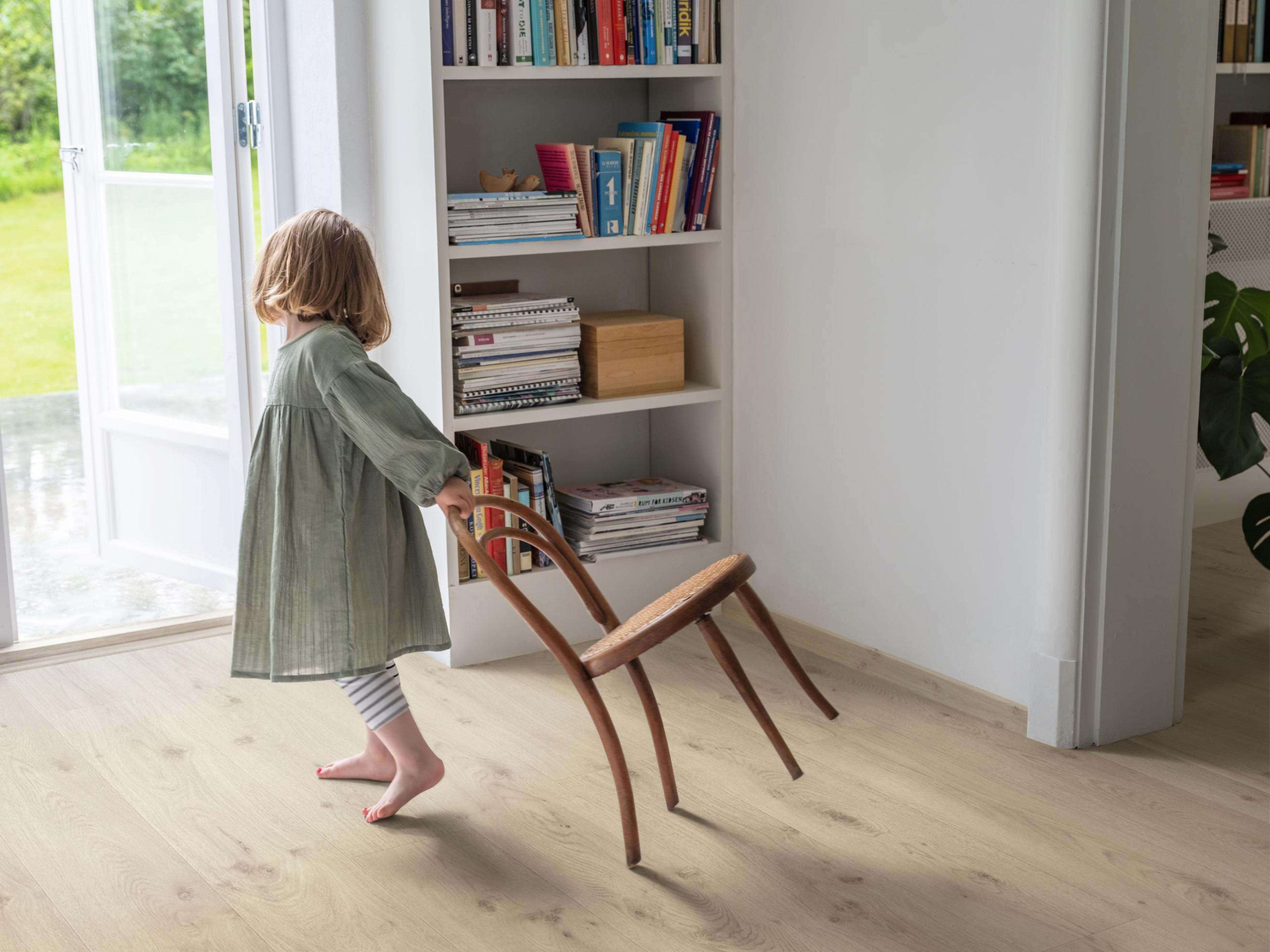 En liten jente som drar en stol etter seg på gulv fra Pergo