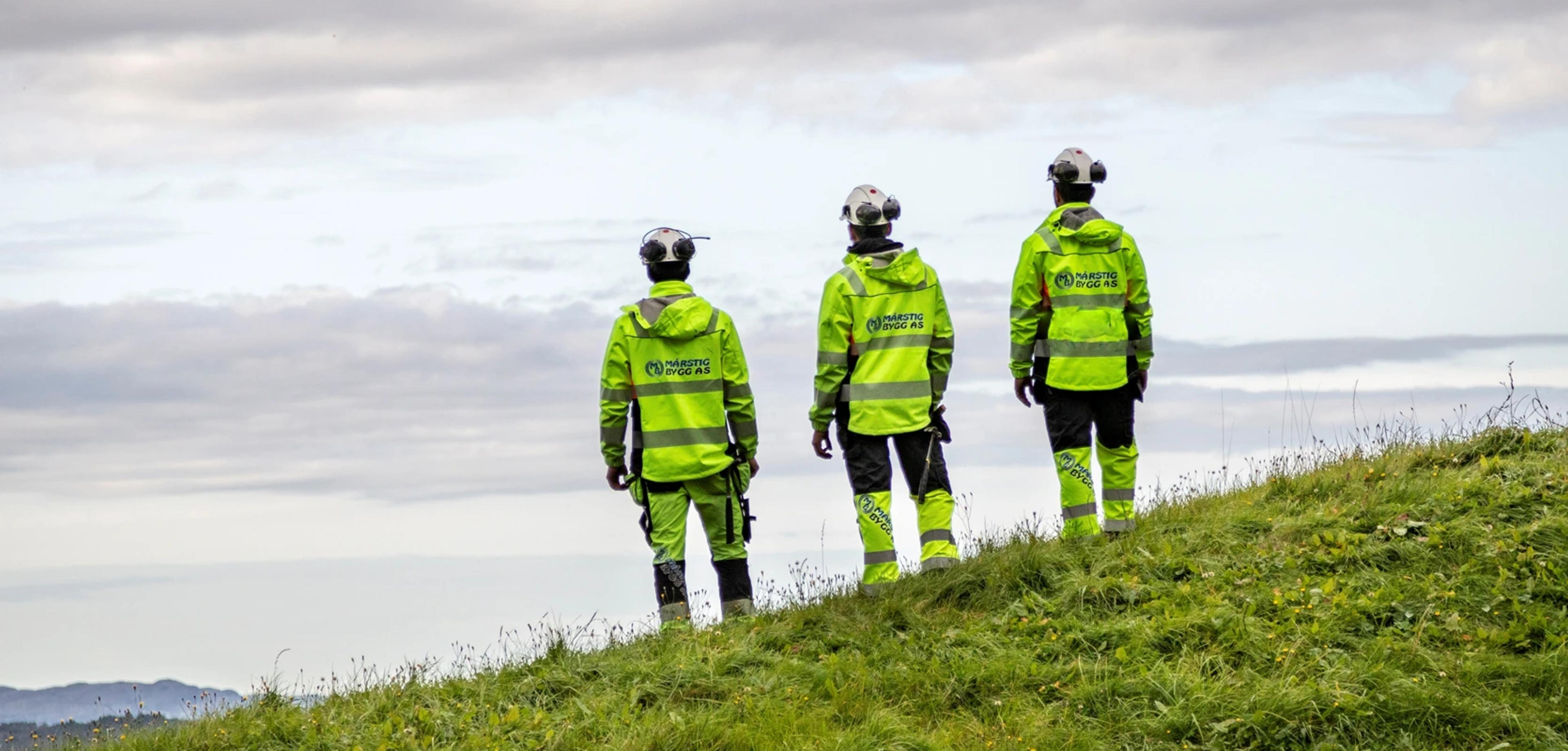 Tre arbeidere med hjelm som ser på horisonten