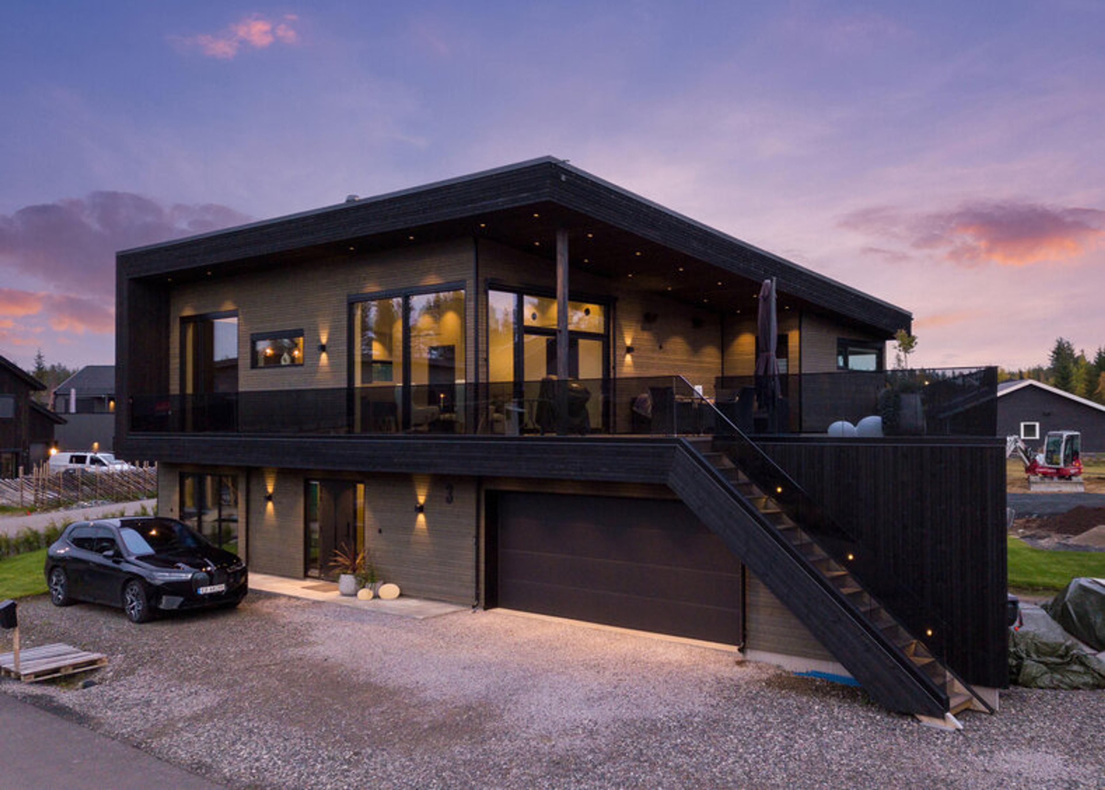 Et mørkebrunt funkishus over to etasjer i kveldsstemning