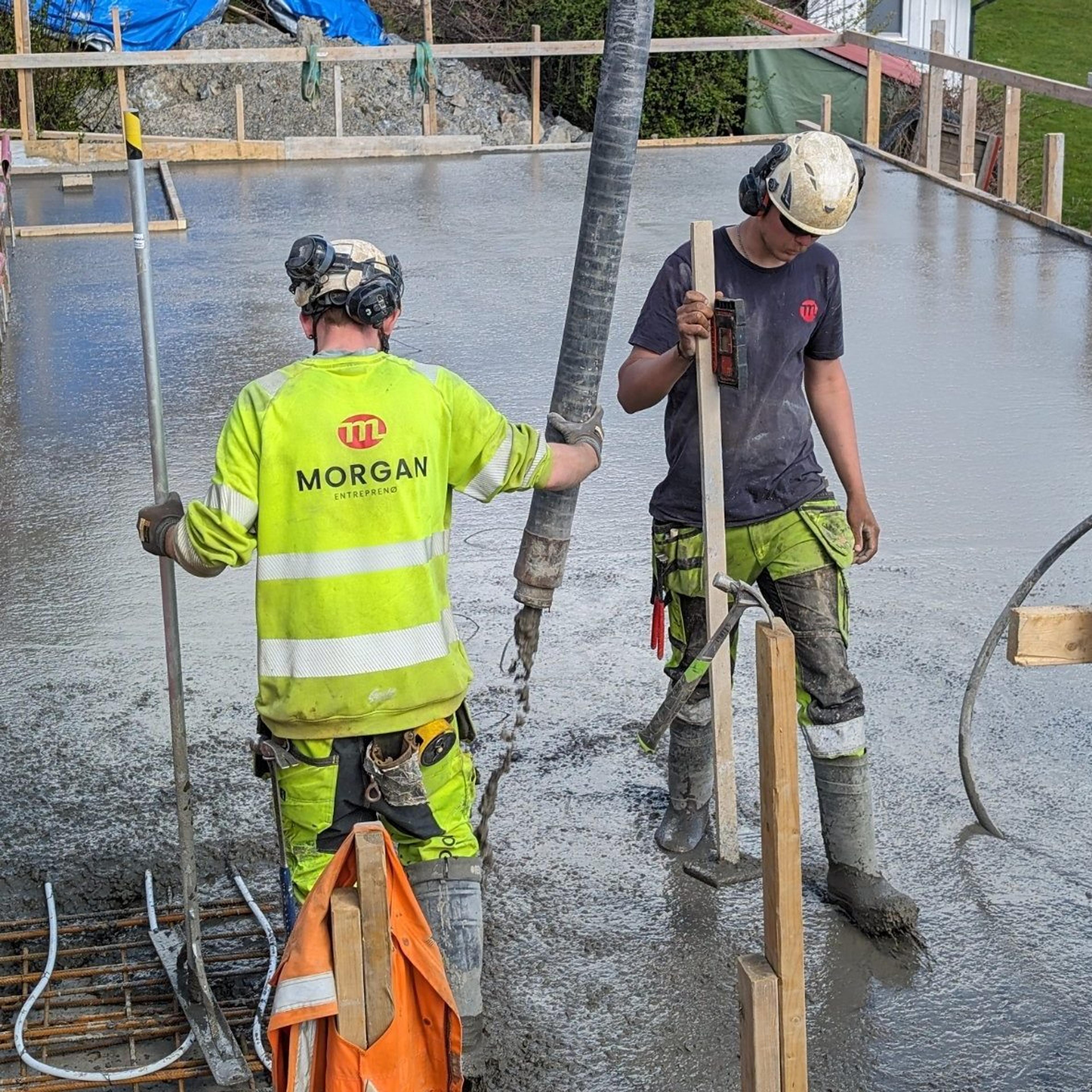 To arbeidere, ene med logo på ryggen som holder et rør