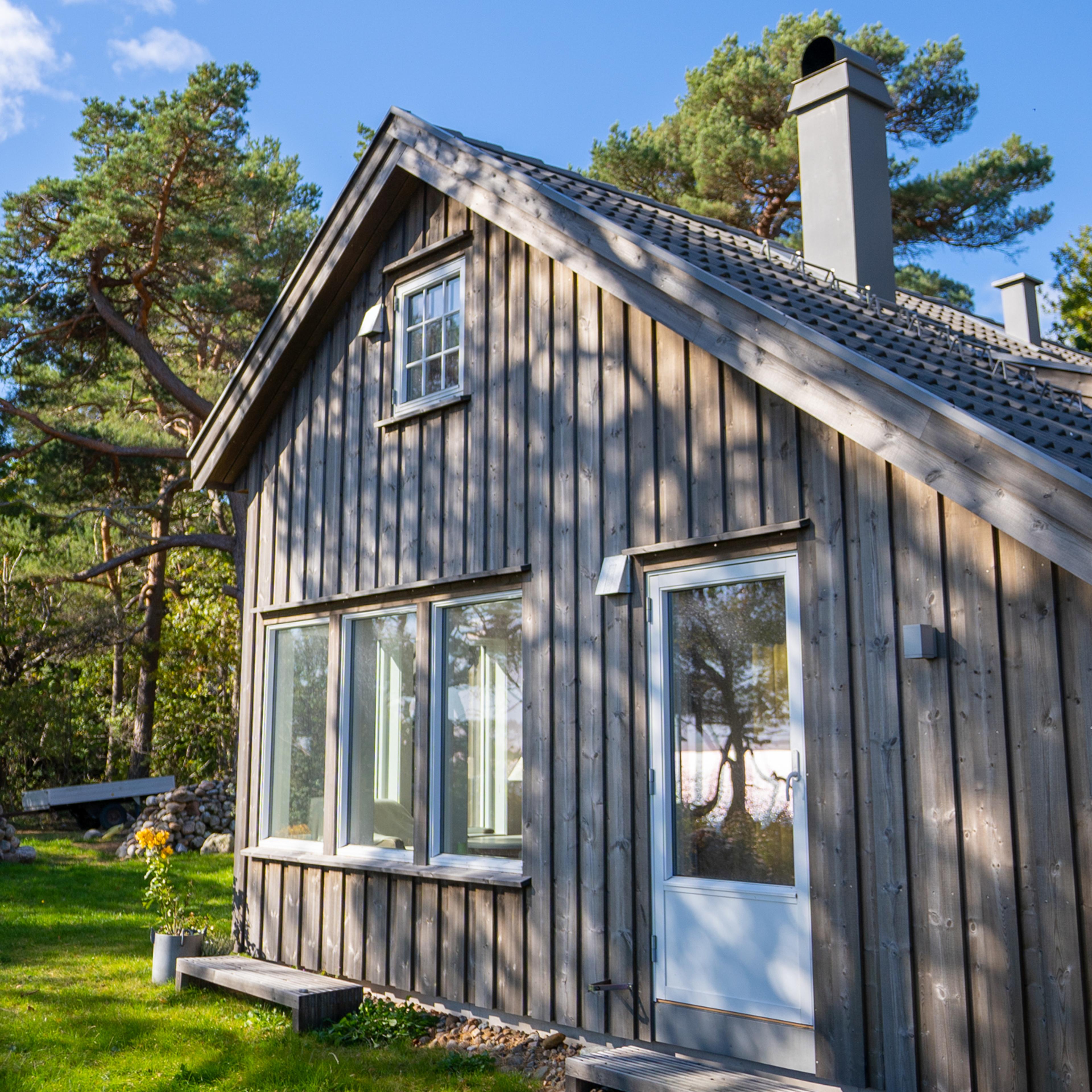 Brun hytte med høye vinduer ved skogen