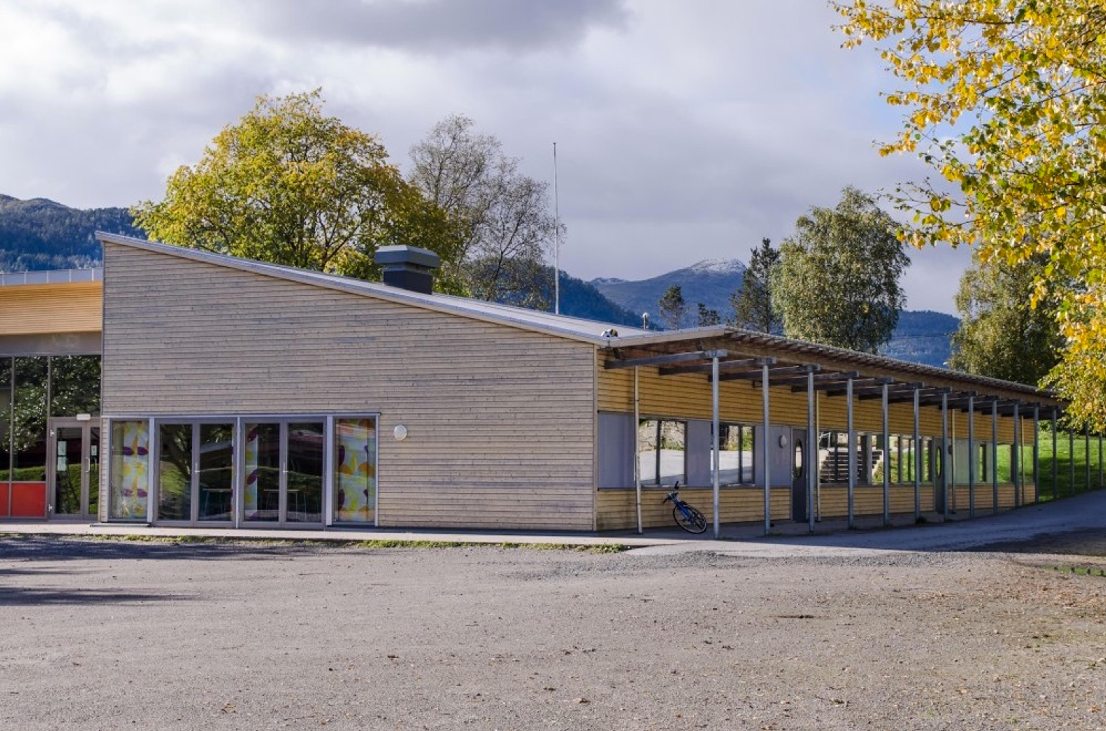 Grå og gul skole med skog og fjell i bakgrunn