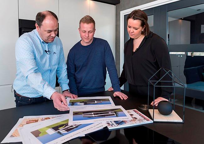 To menn og en kvinne står lent over noen huskataloger på en kjøkkenbenk