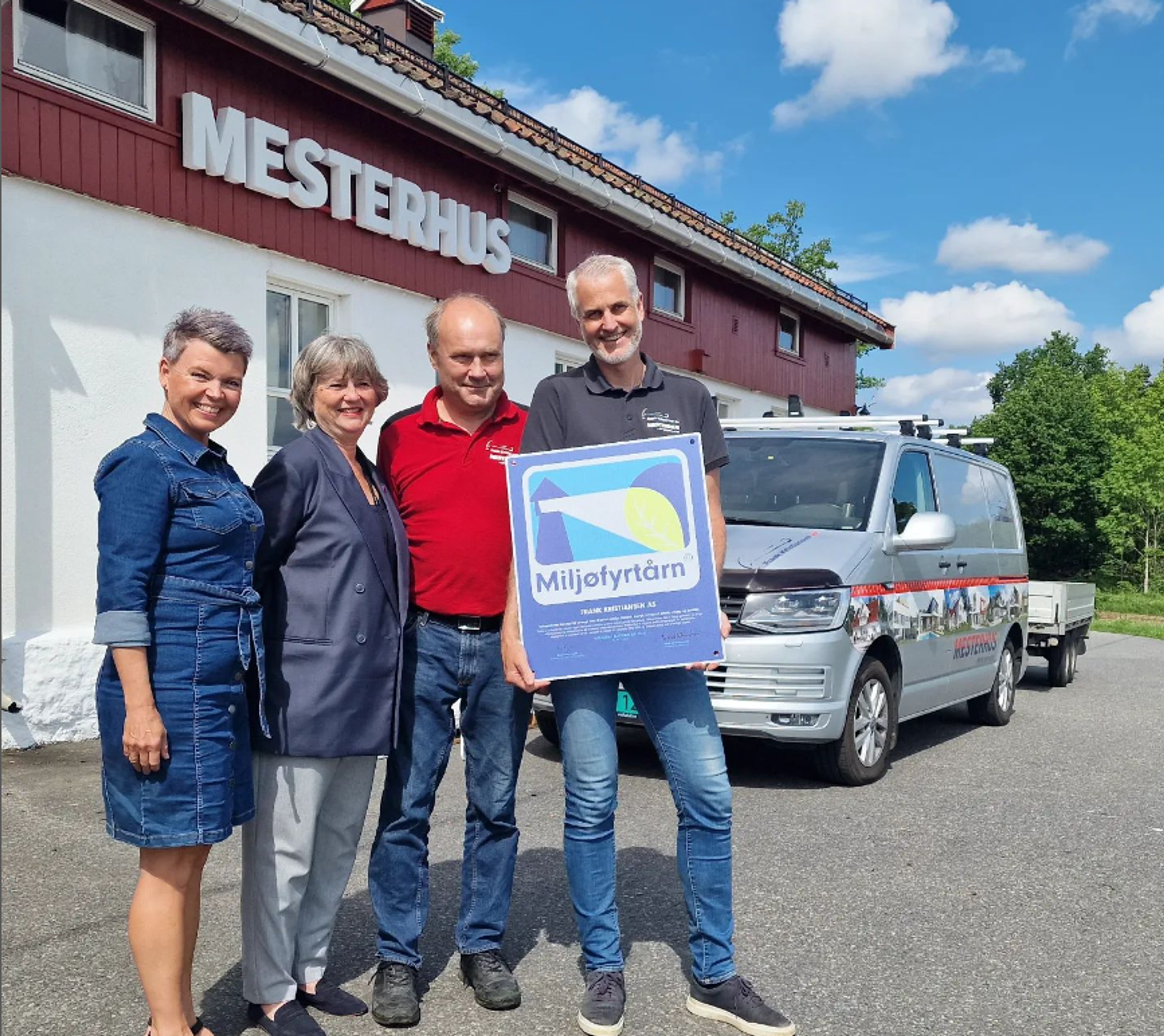 Fire arbeidere utenfor firmahus som holder miljøfyrtårnplakat