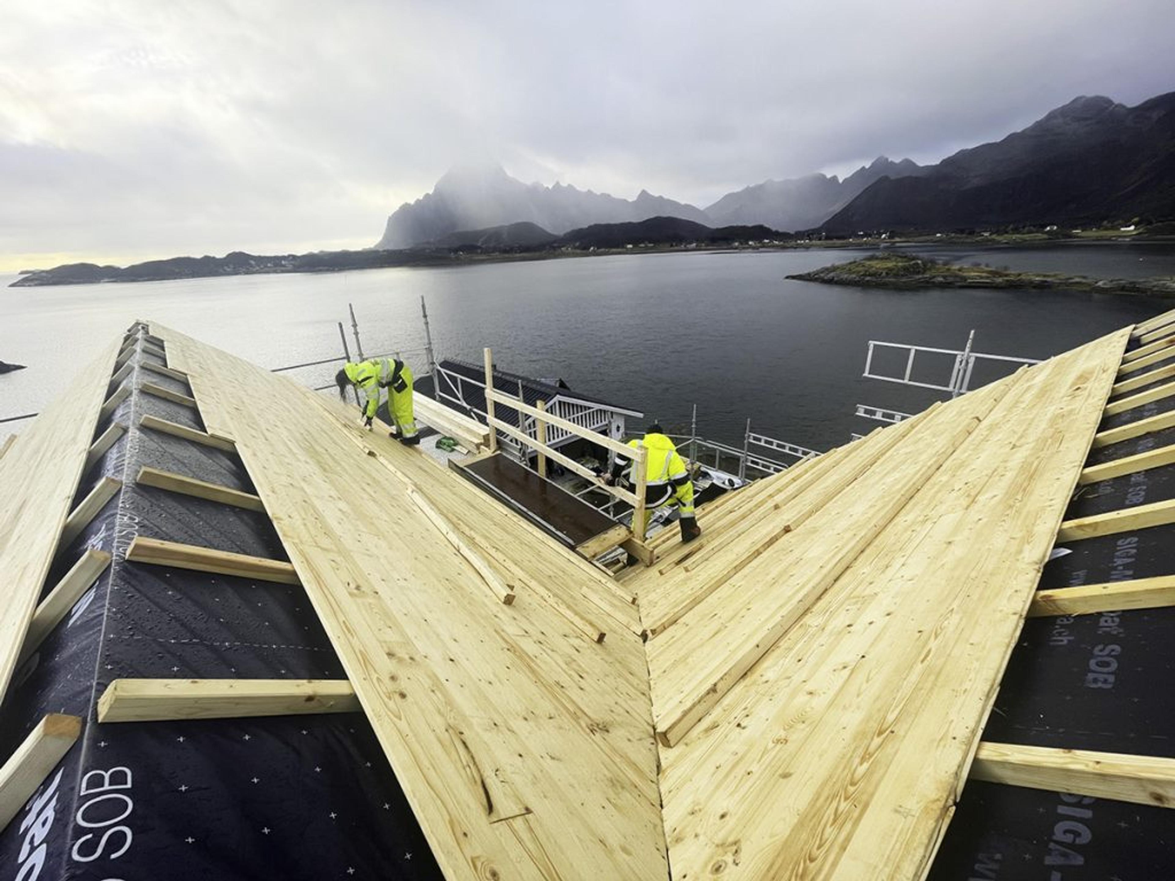 To arbeidere som jobber på taket av en badstue ved havet