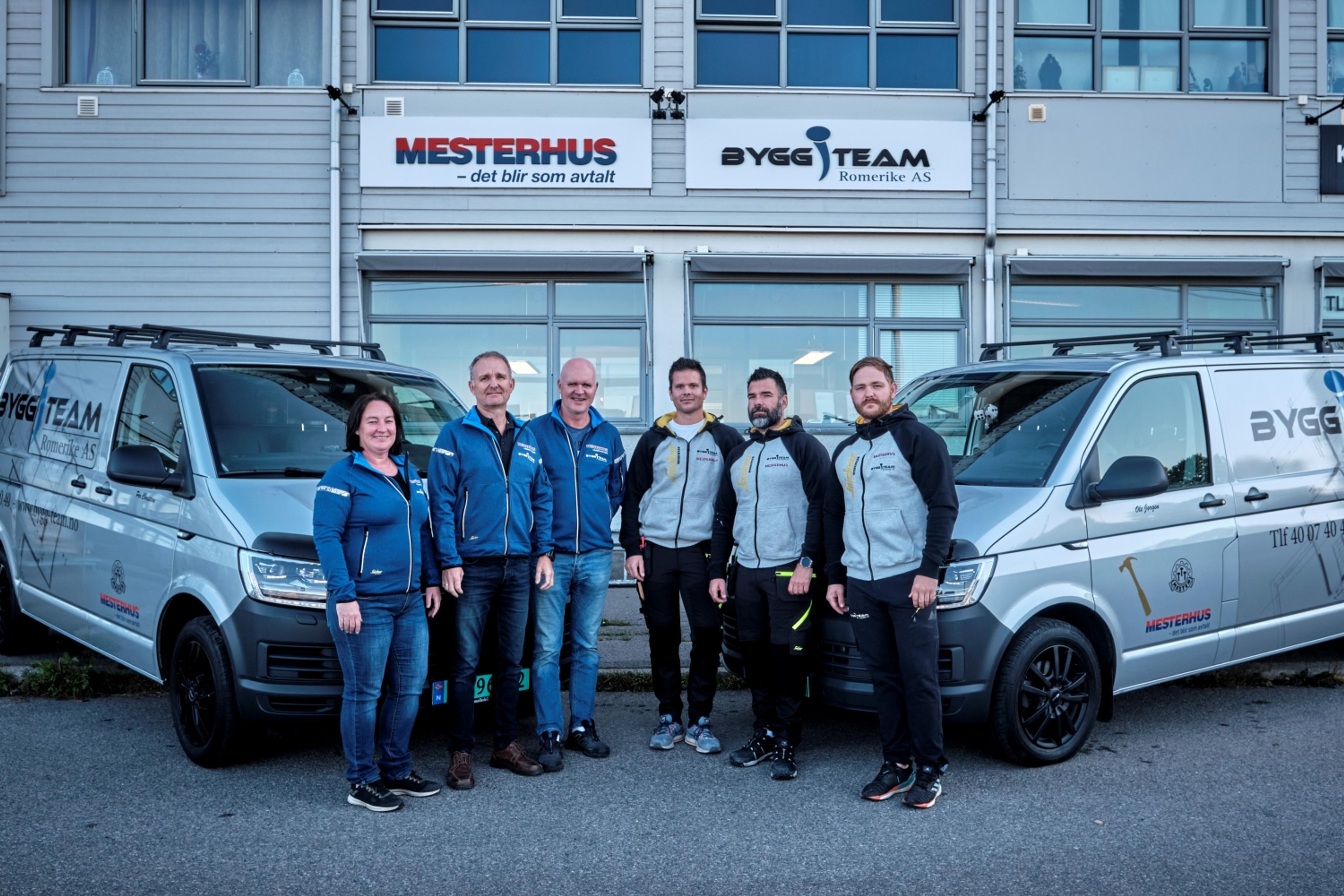 Ansatte gruppebilde med firmabiler og firmabygg i bakgrunn