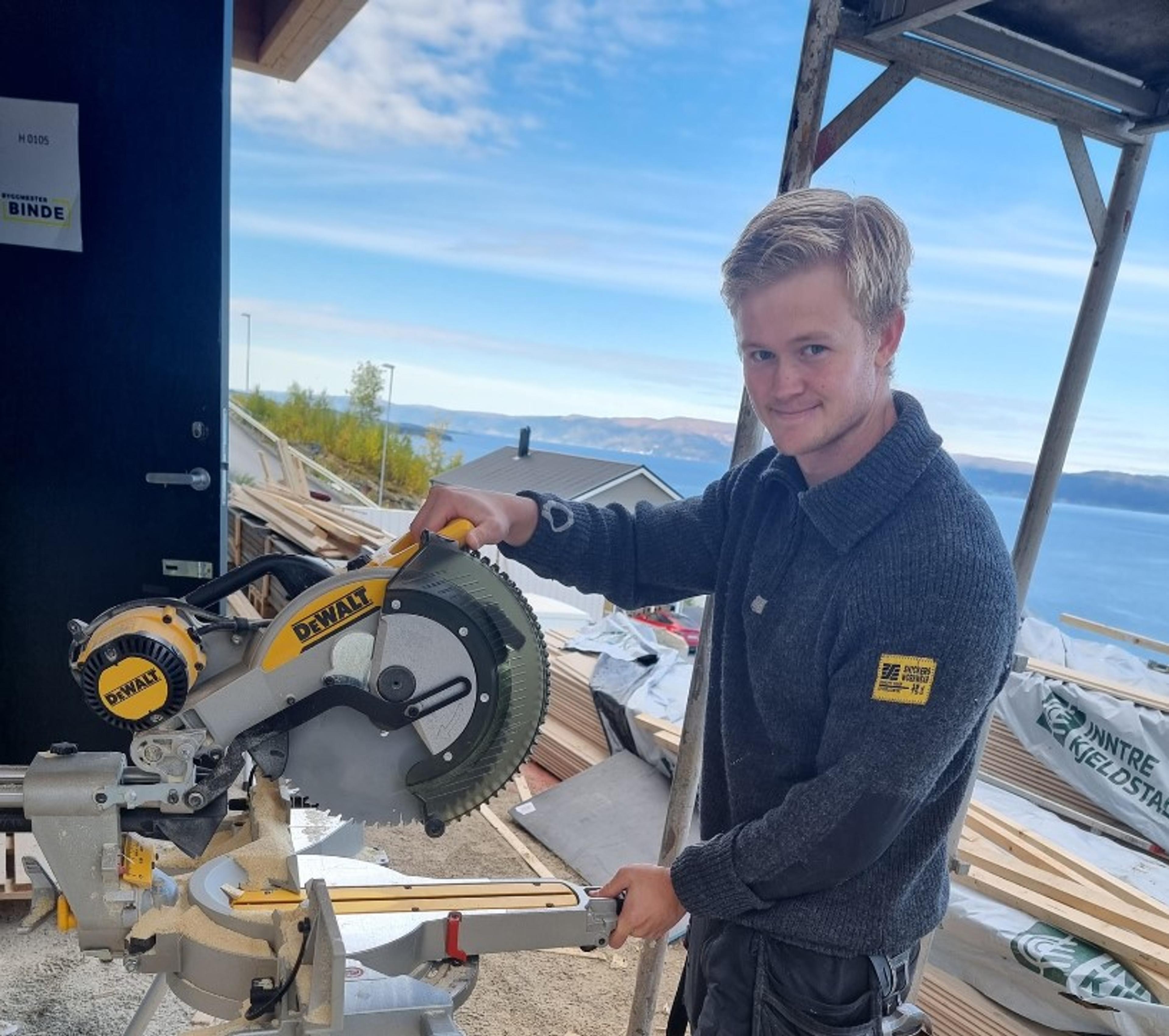 Arbeider med elektronisk sag med sjø i bakgrunn
