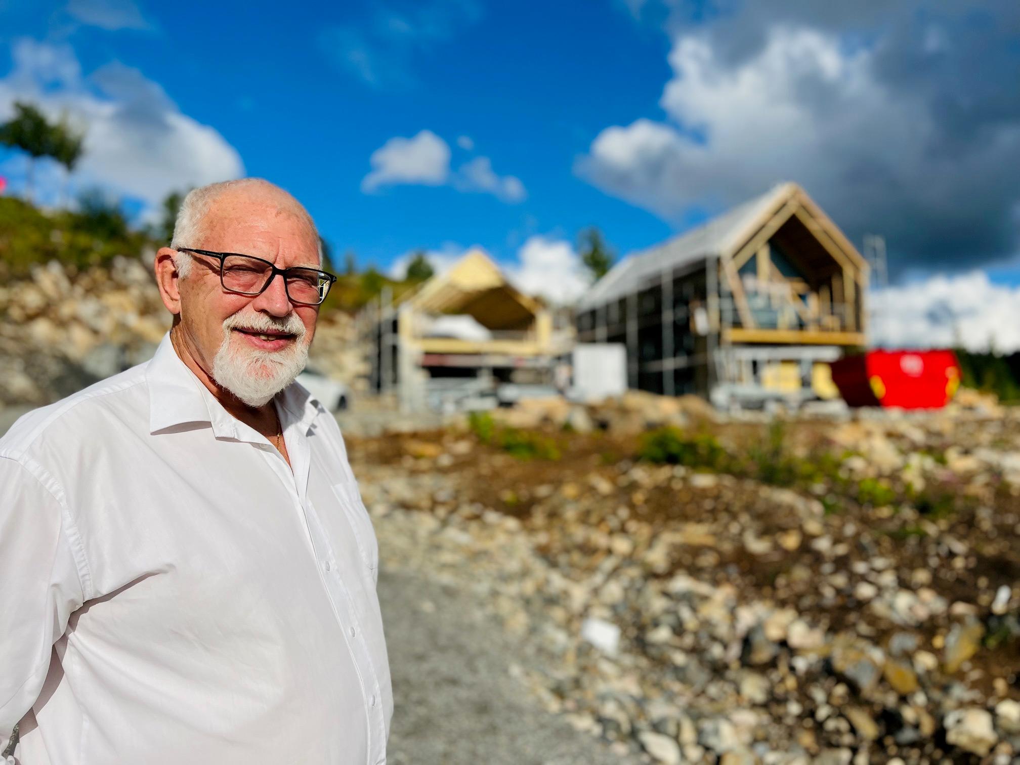 En mann i hvit skjorte står ved siden av en byggeplass