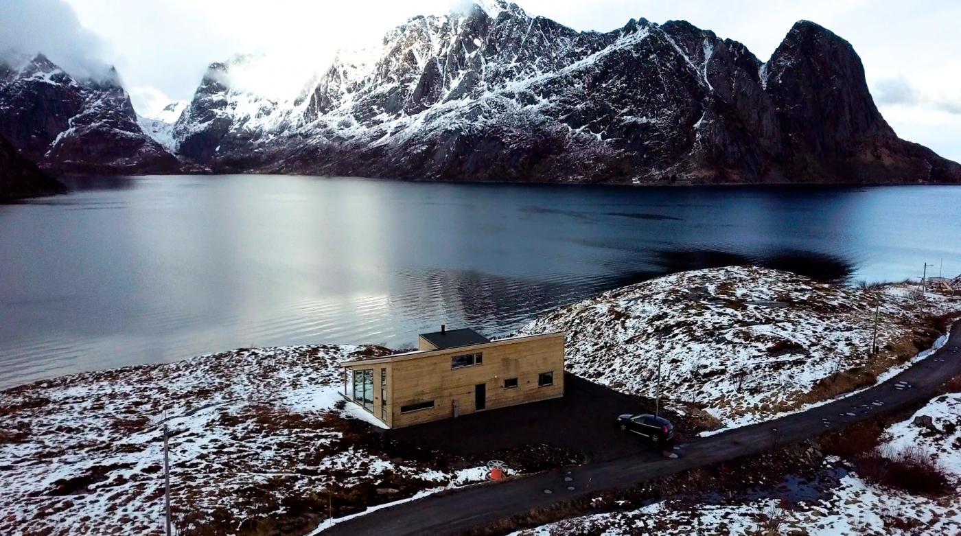 Et hus langs havet med store fjell med snø rundt