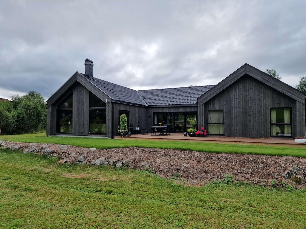 Atriumhus med mørkegrå fasade og store vinduer med stor plen og jordet foran huset.