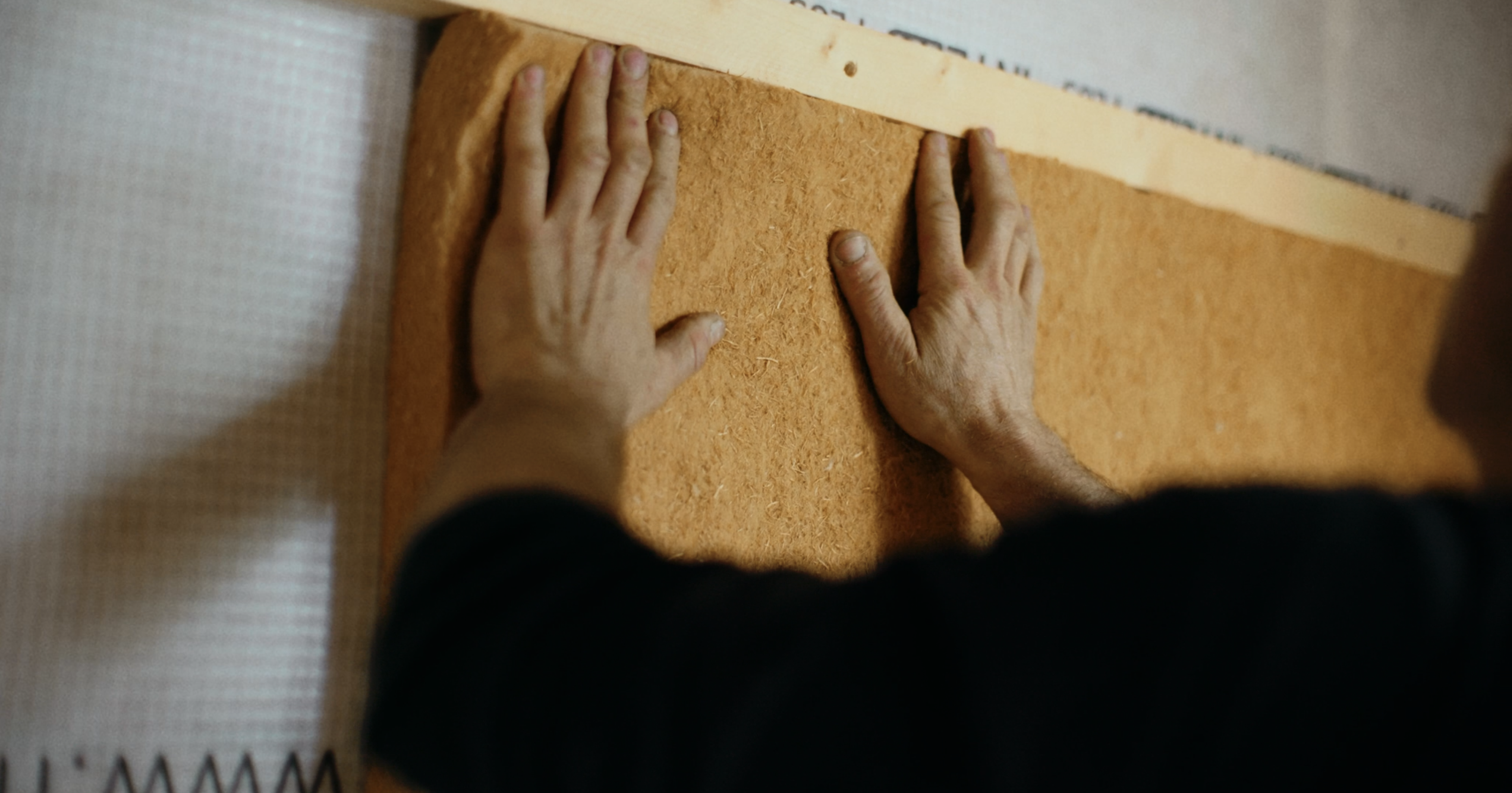 Mann som legger trefiberisolasjon i vegg