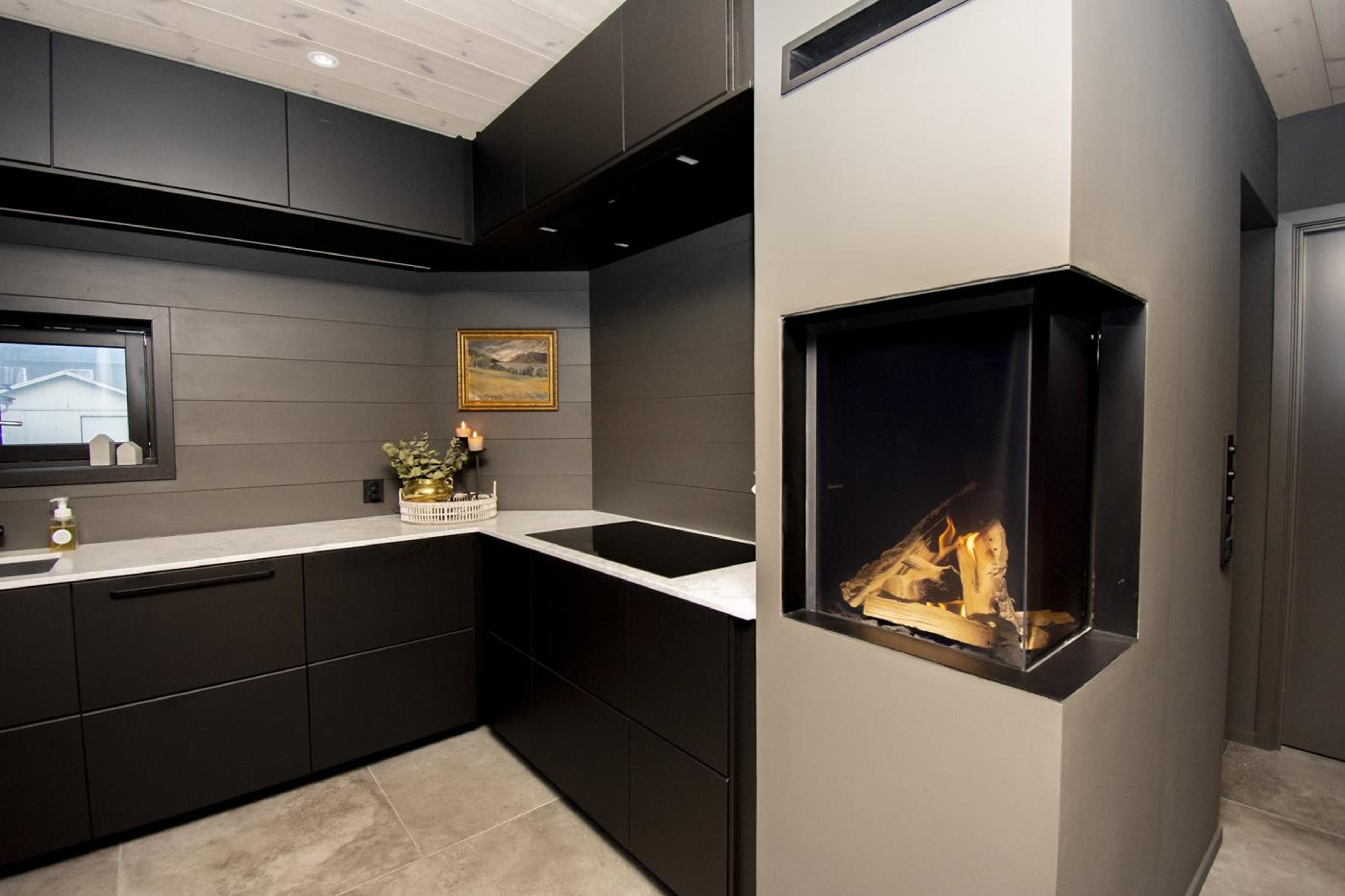 Stilrent kjøkken med svarte fronter og grå vegg og peis