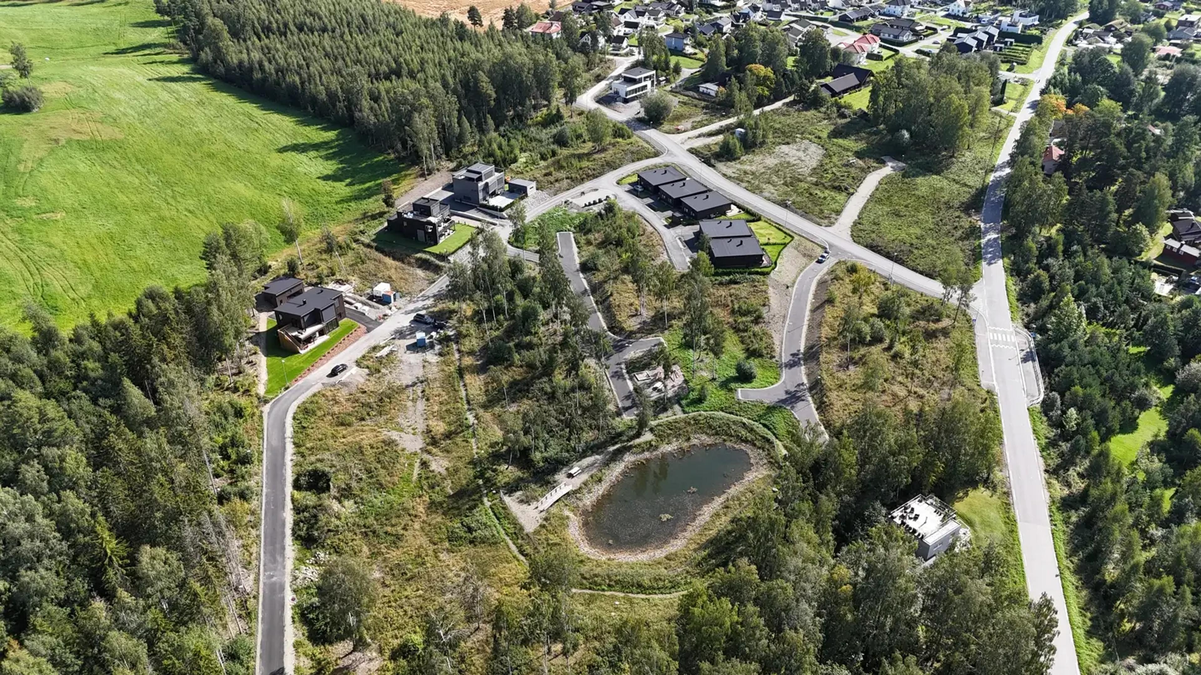 Oversiktsbilde over boligfeltet med et jordet bak og en dam inne på feltet.