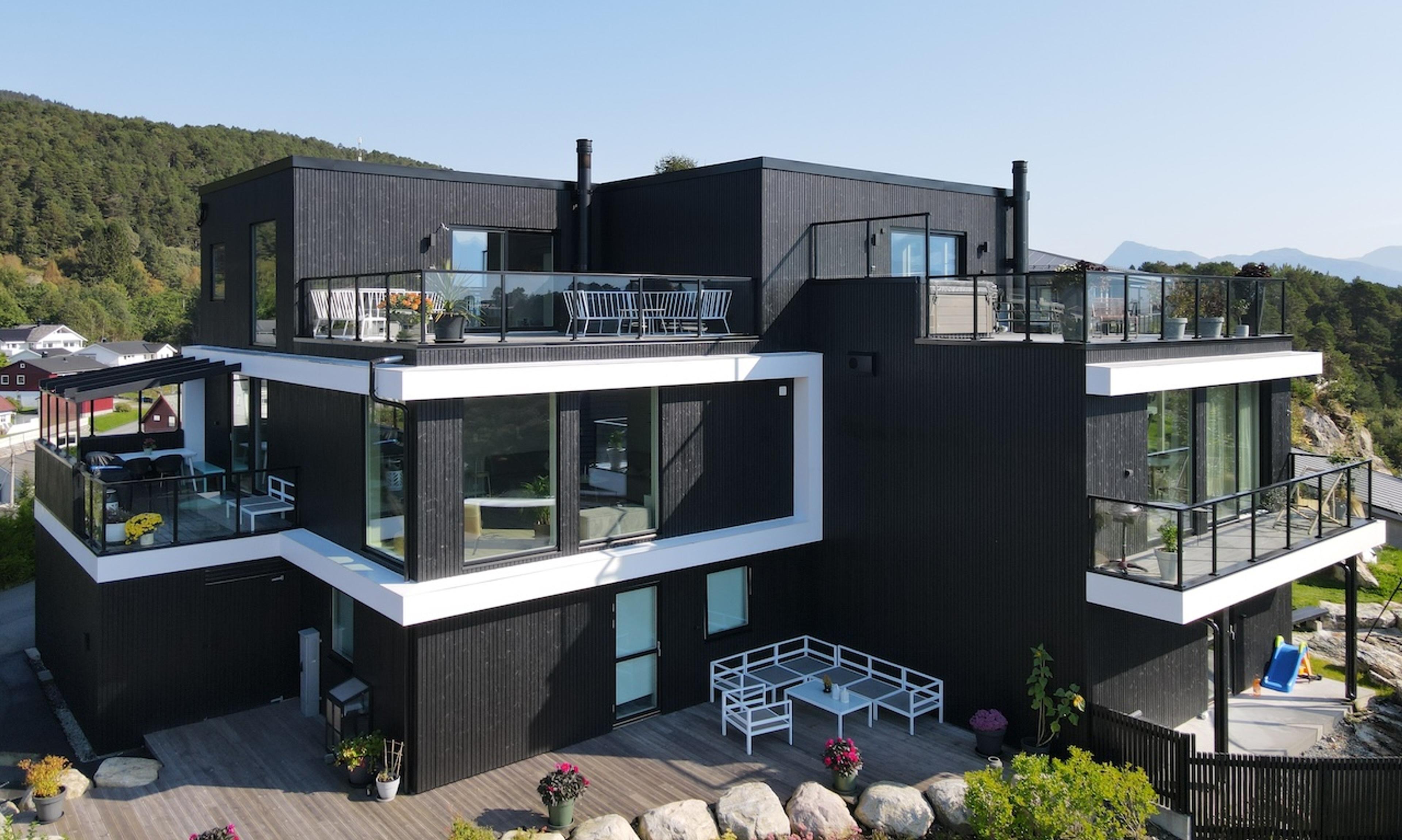Arkitekttegnet tomannsbolig over tre etasjer med veranda, takterrasse, svart kledning og hvite detaljer.