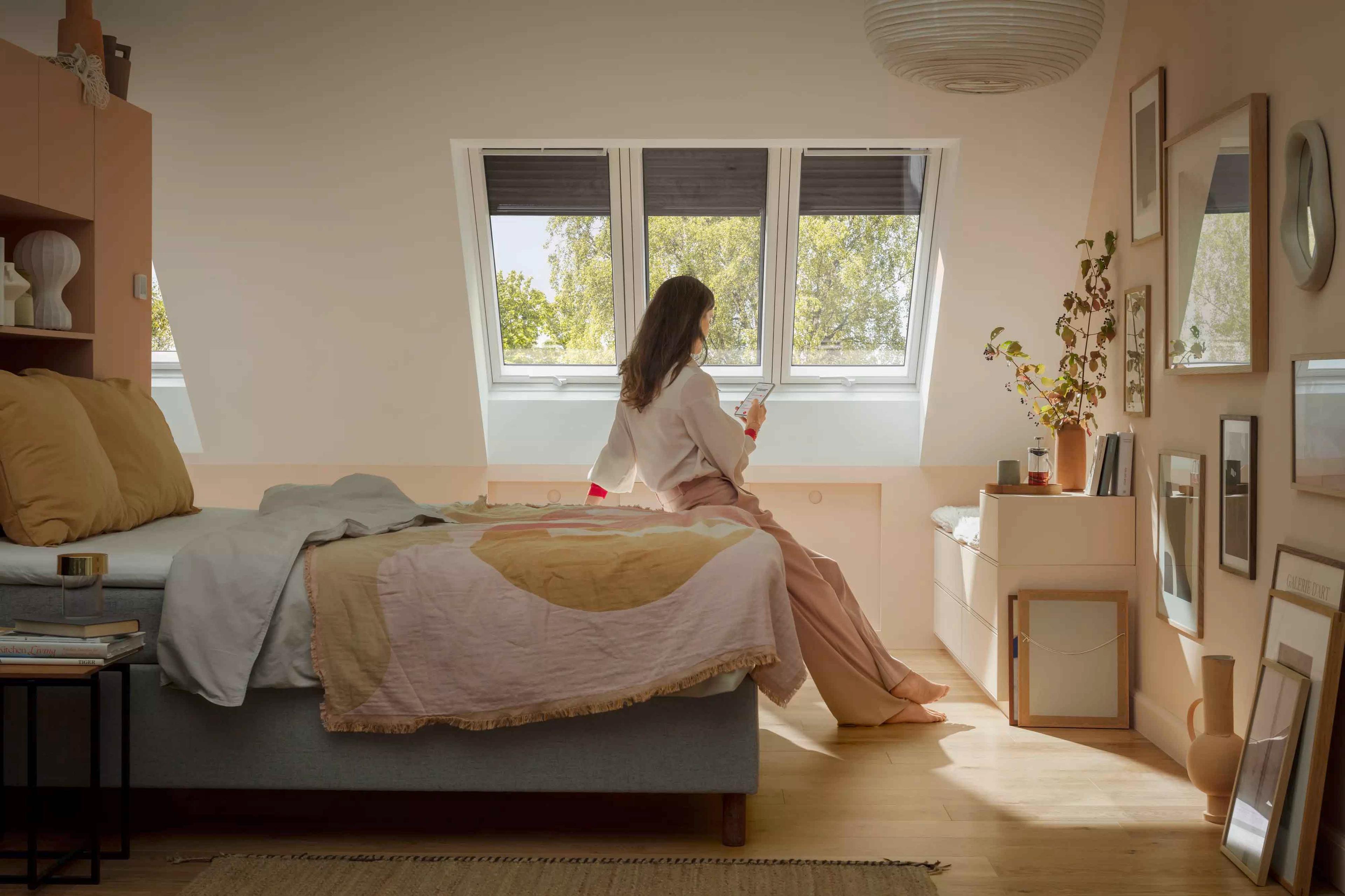En jente som sitter på sengen under et stort takvindu fra Velux