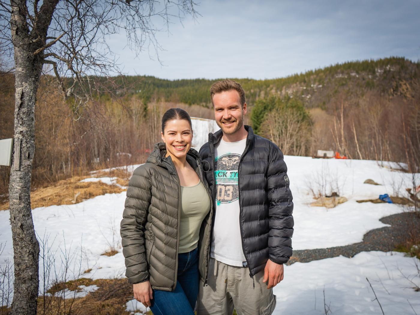En mørkhåret dame i hestehale og en mørkhåret mann står ved en tomt