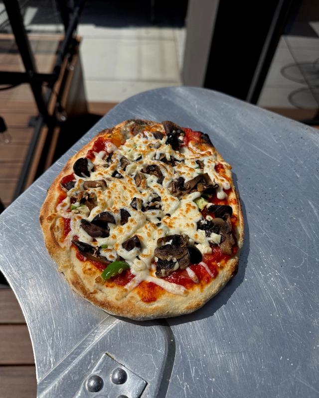 A mushroom and olive pizza on a metal peel in bright sunlight