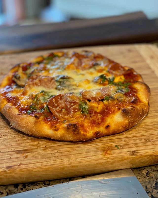A salami pizza with herbs and mushrooms on a wooden cutting board in the kitchen
