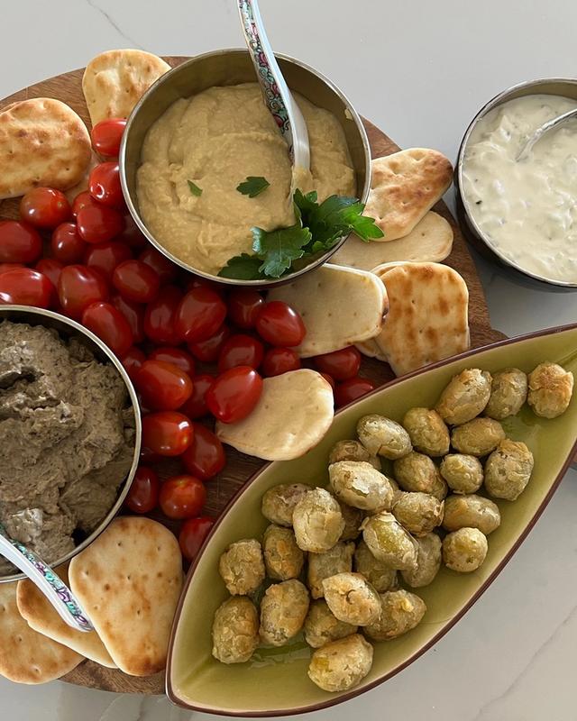 A board of dips — hummus, a dark aubergine dip and a herbed yoghurt — with warm flatbread, cherry tomatoes and stuffed olives