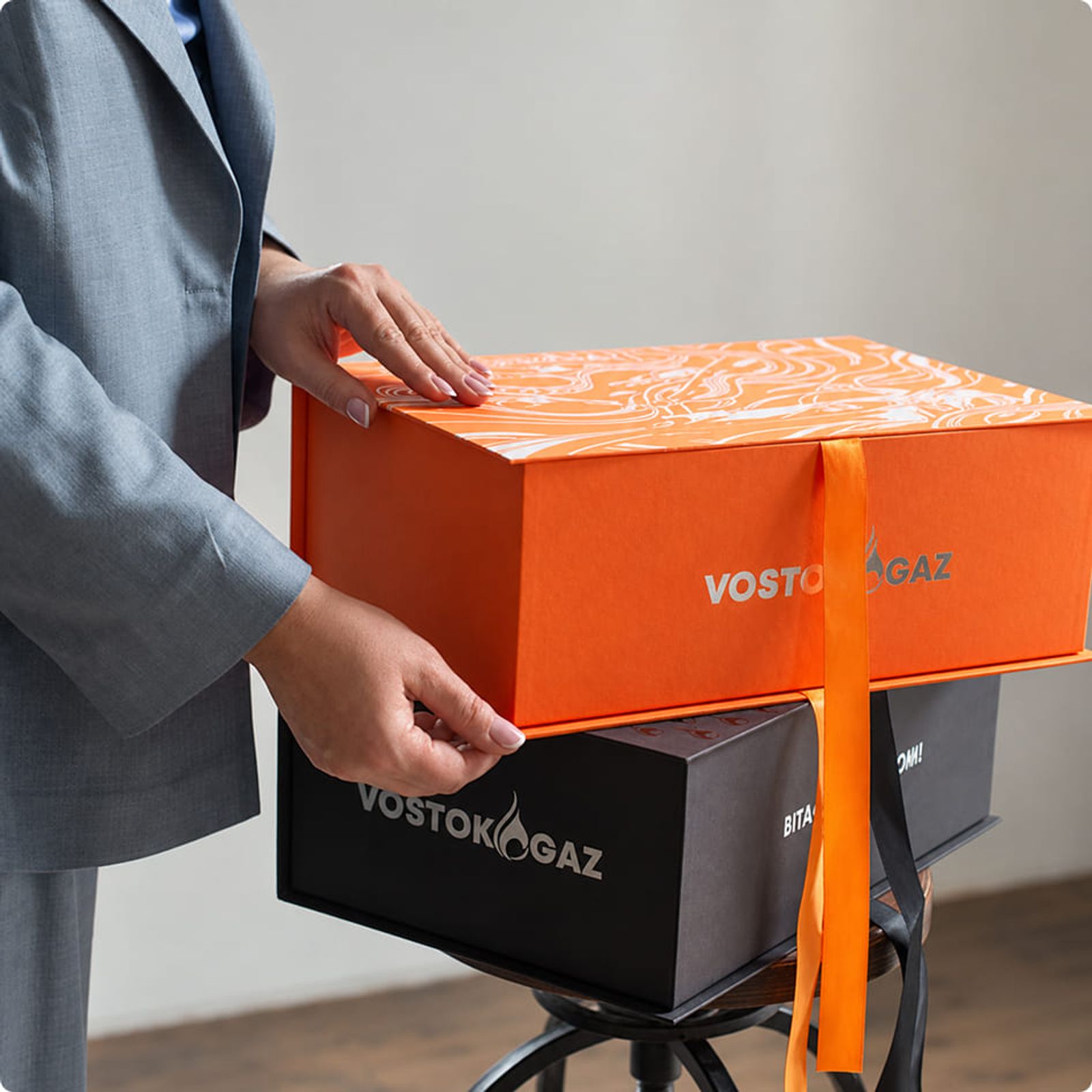 Person mit einem orange-schwarzen, hochwertig verpackten Geschenk als individuelles Mitarbeitergeschenk.