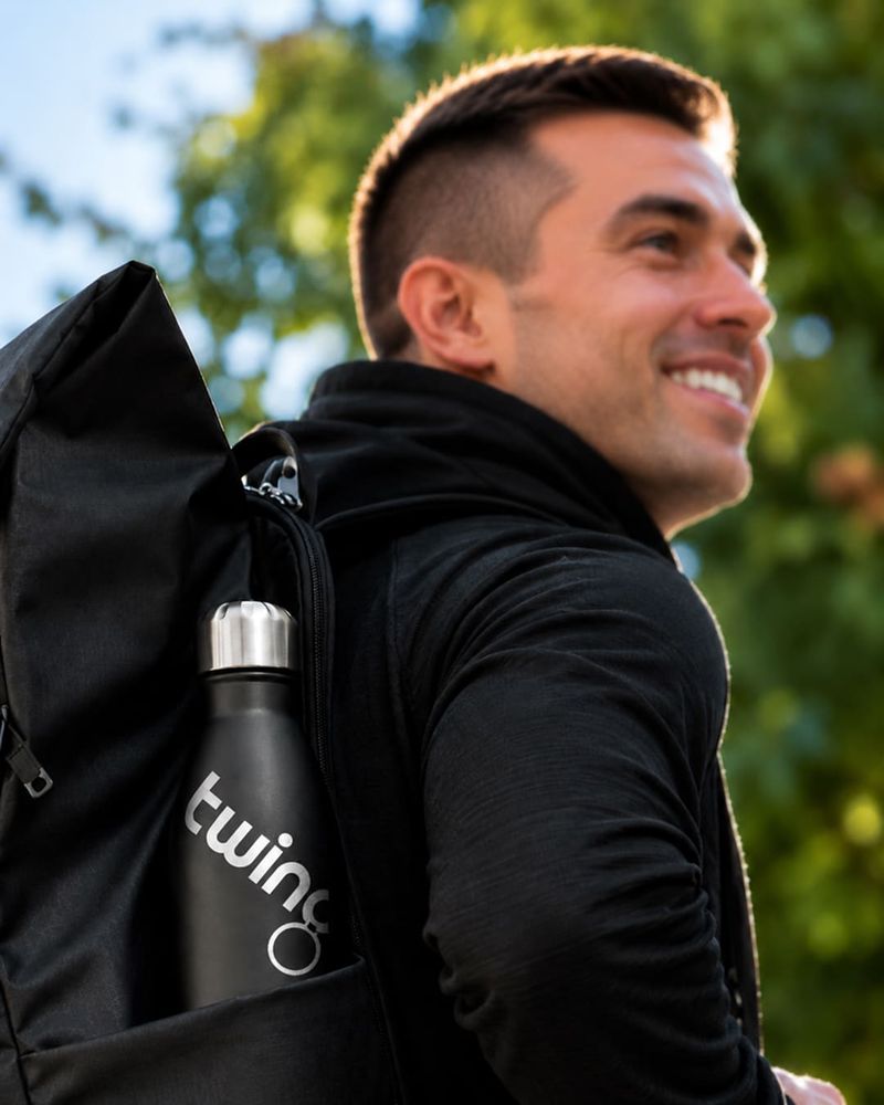 Schwarze Trinkflasche mit silbernem Firmenlogo bedruckt in der Seitentasche eines Rucksacks