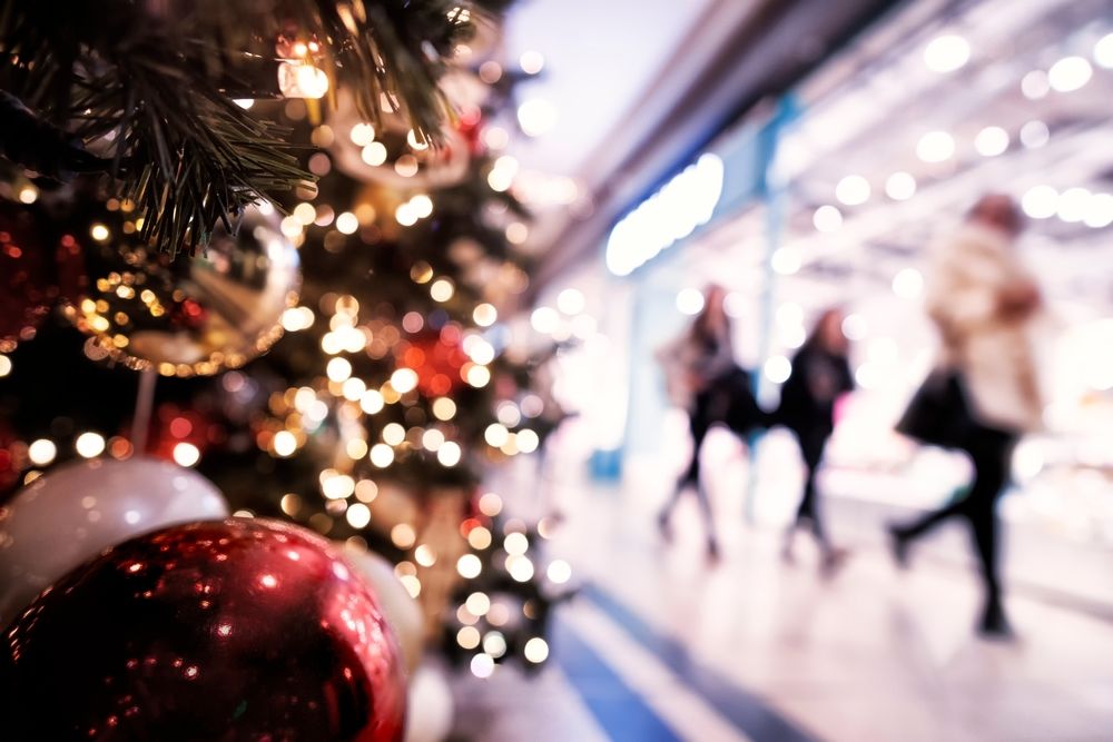 Holiday shopping mall with Christmas tree decorations and blurred shoppers walking through crowded aisles, illustrating potential slip and fall hazards during the holidays.