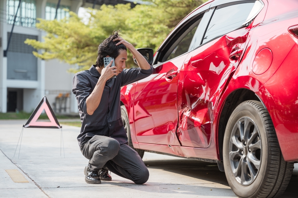 Image Driver on phone inspecting damage to red car after accident, illustrating common insurance adjuster mistakes after a Pennsylvania car crash