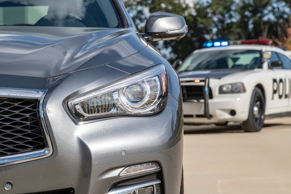 Image Close-up of a grey car being pulled over by a police cruiser with blue lights flashing during a DUI stop.