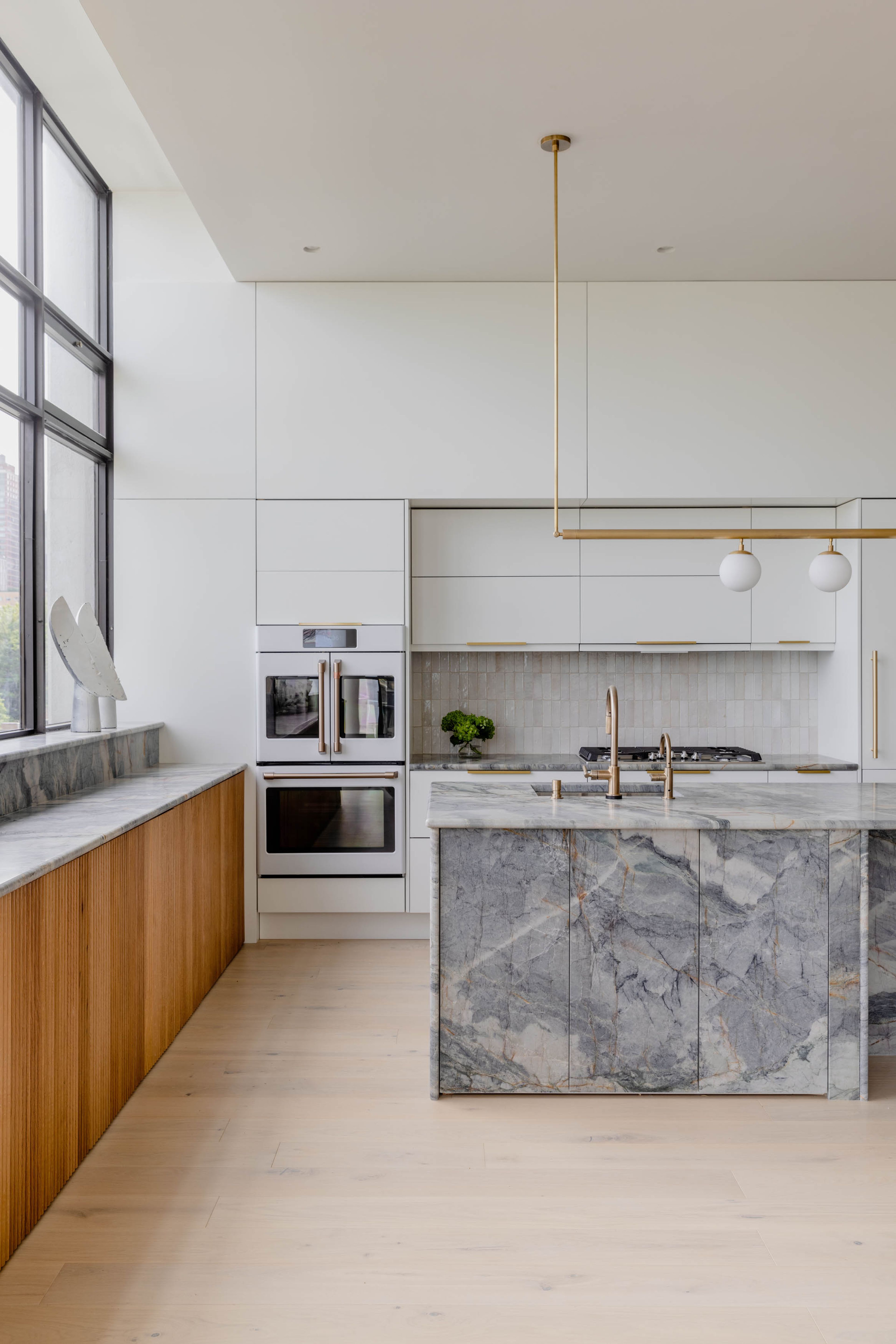 View of the oven betwixt fluted wood and quartzite stone island.